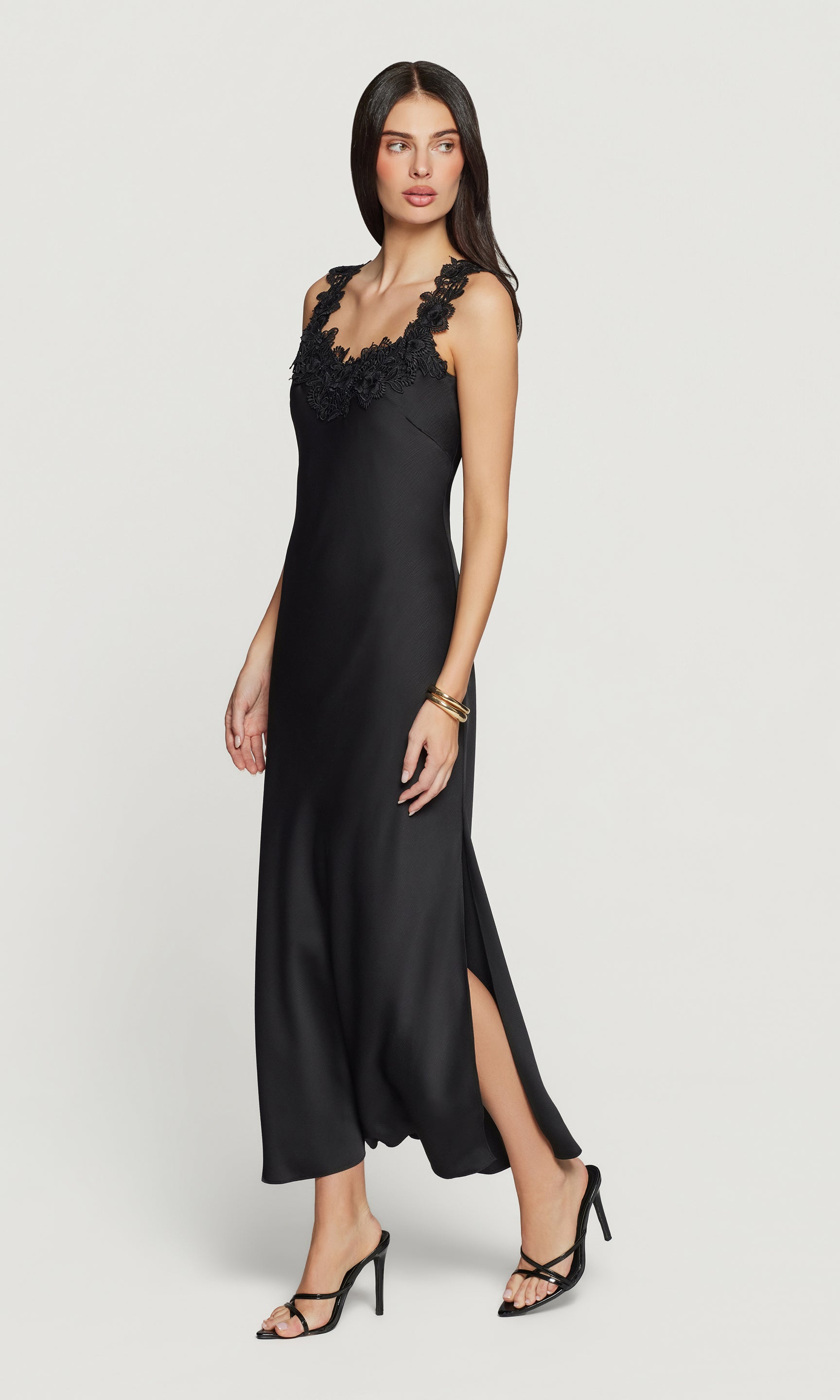 Side view of woman wearing a black satin dress with lace details on a white background