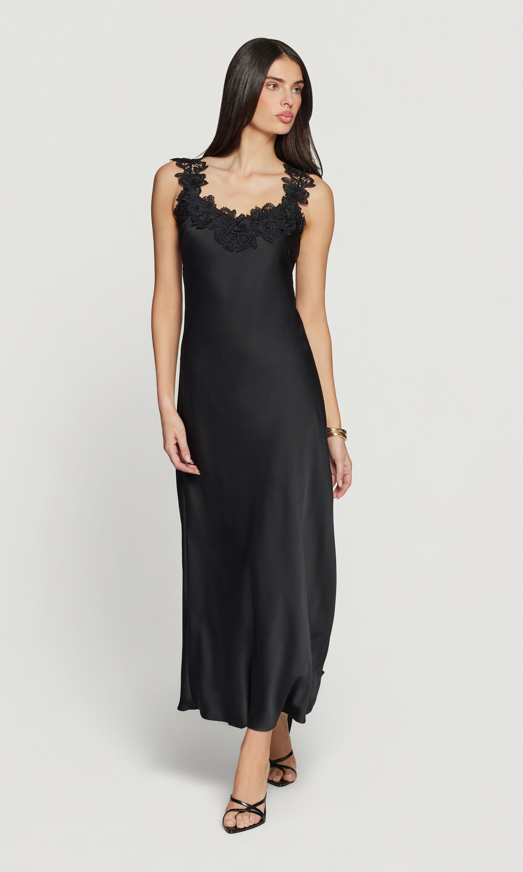Woman wearing a black slip dress with lace detailing on a white background