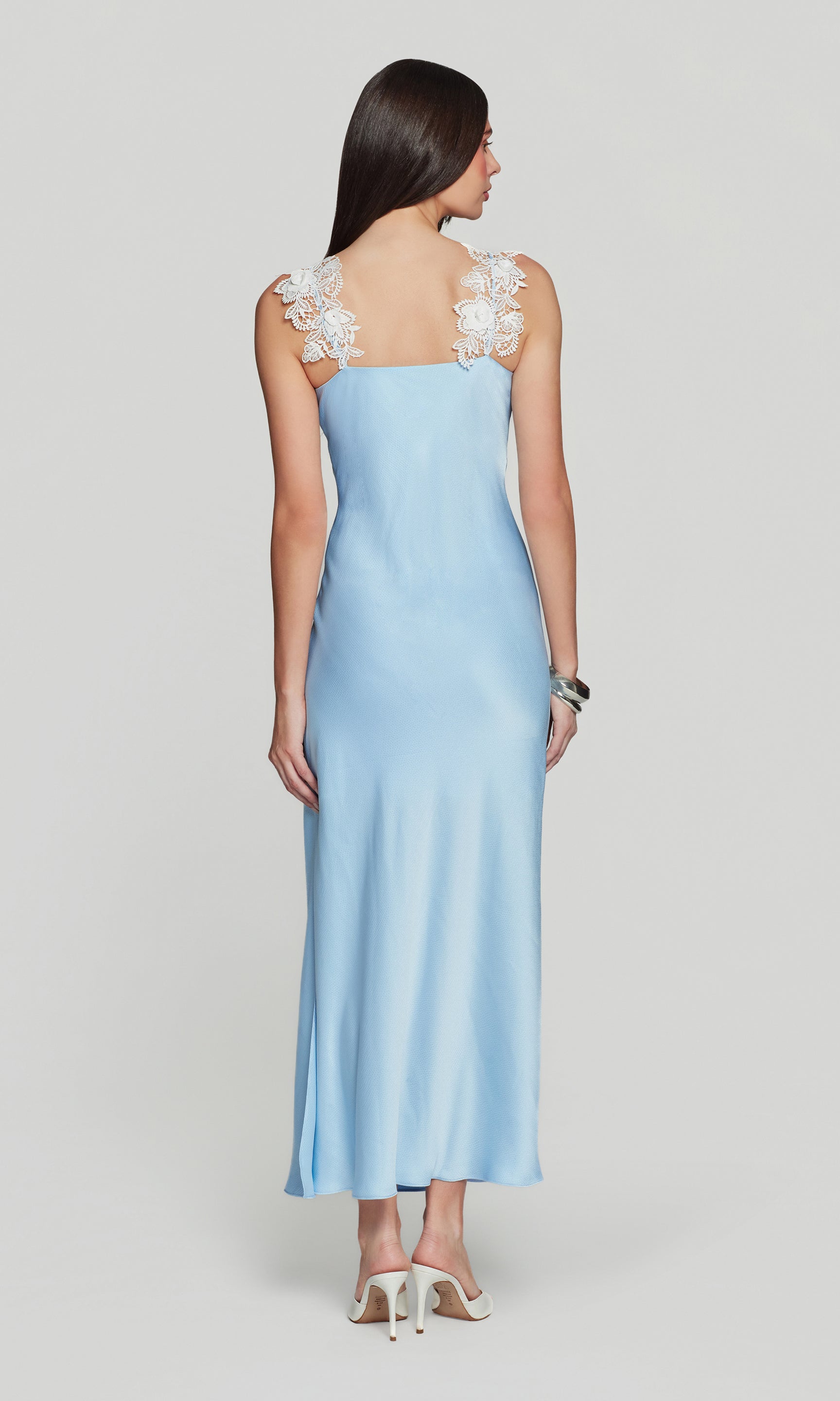 Back view of woman wearing a light blue dress with lace straps on a white background
