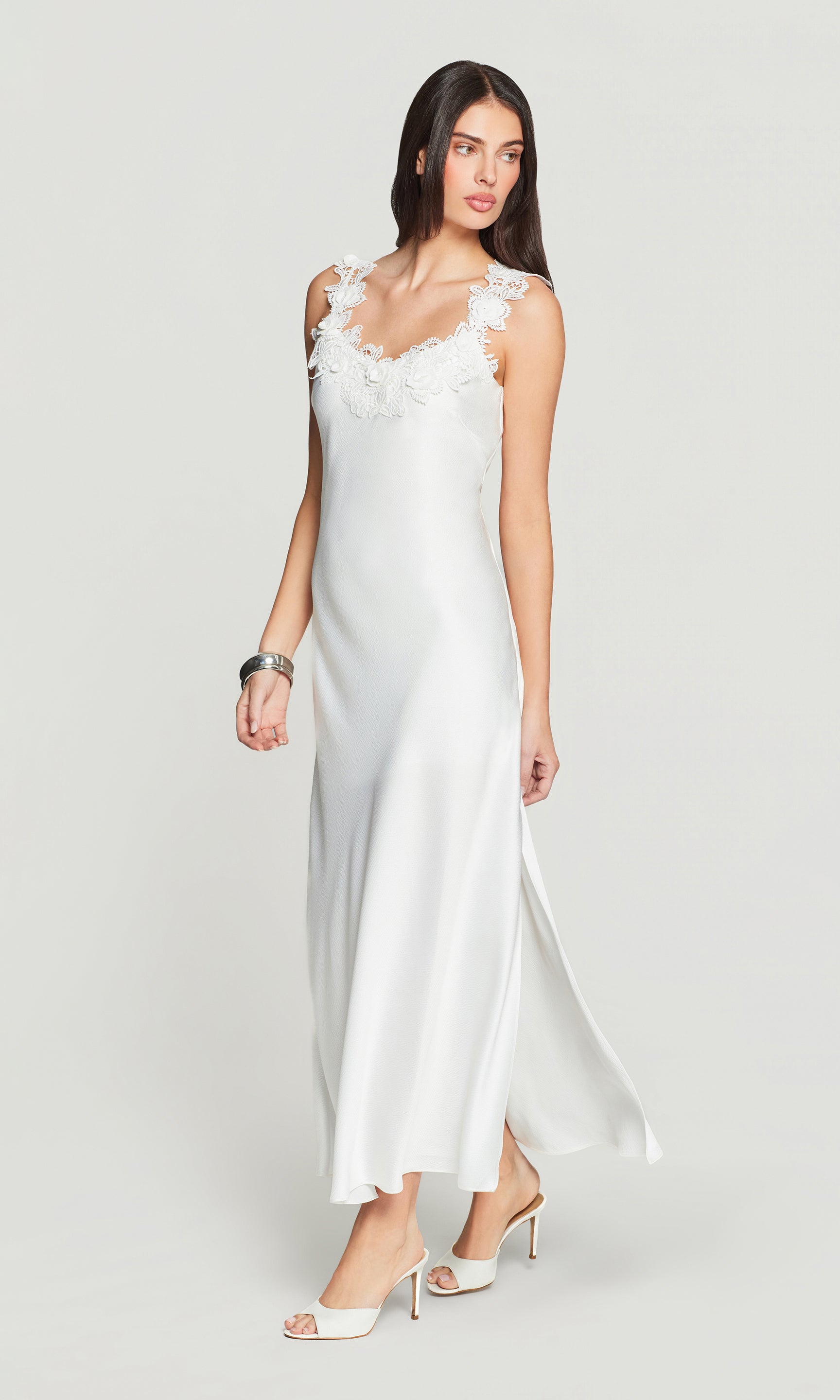 Side view of woman wearing a white dress with floral lace details on a plain background