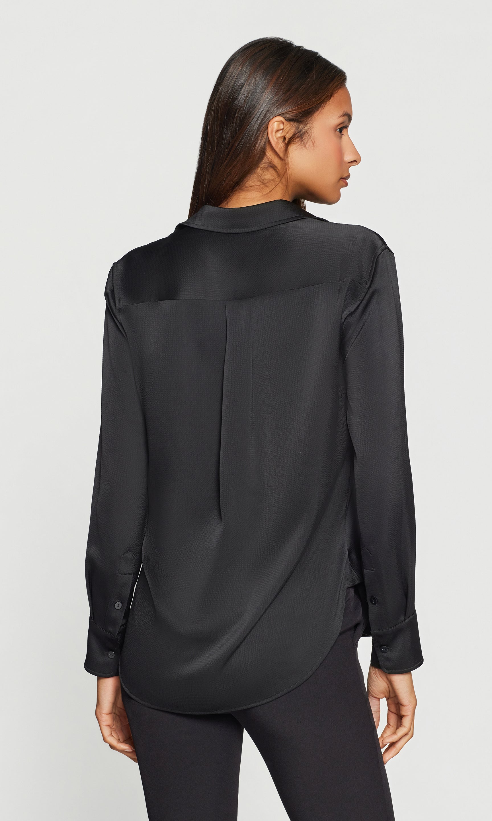 Back view of woman wearing a black satin blouse on a white background