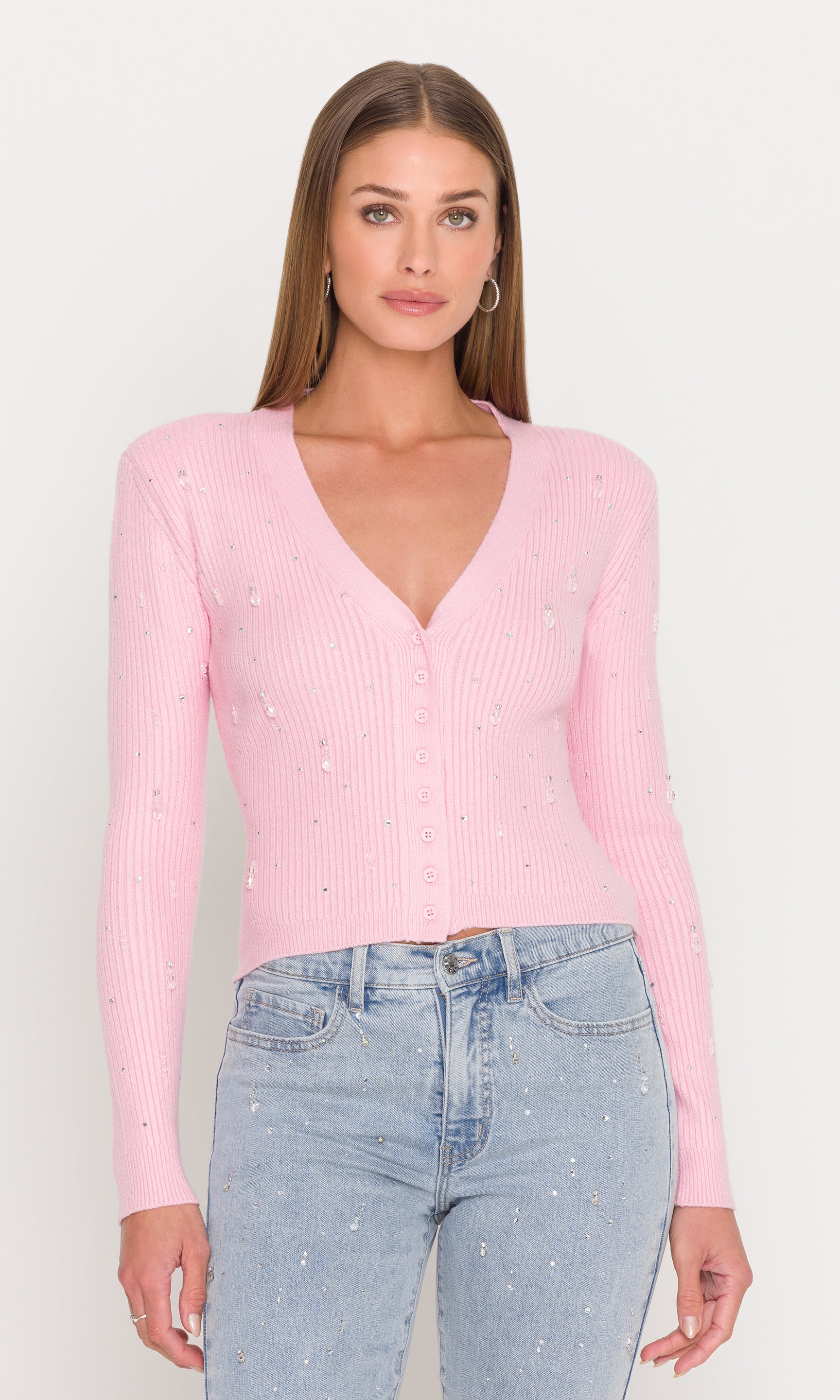 Woman wearing a pink ribbed sweater and light blue jeans on a white background