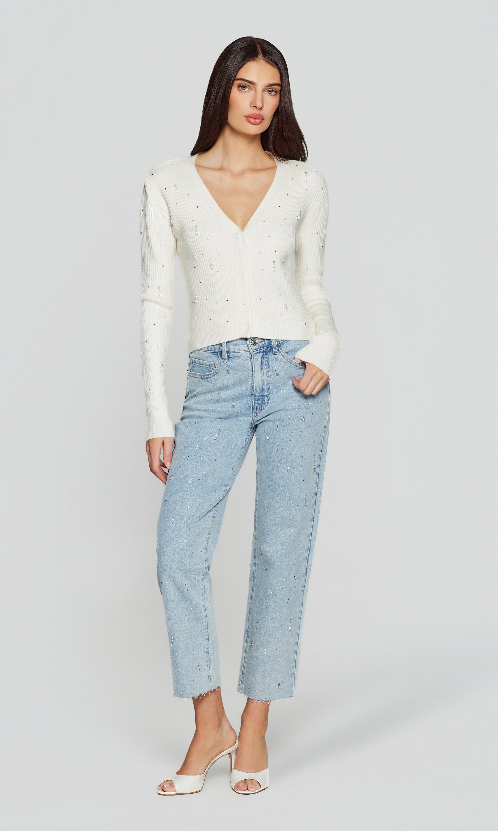 Full body view of woman wearing a white sweater and light blue jeans on a plain background