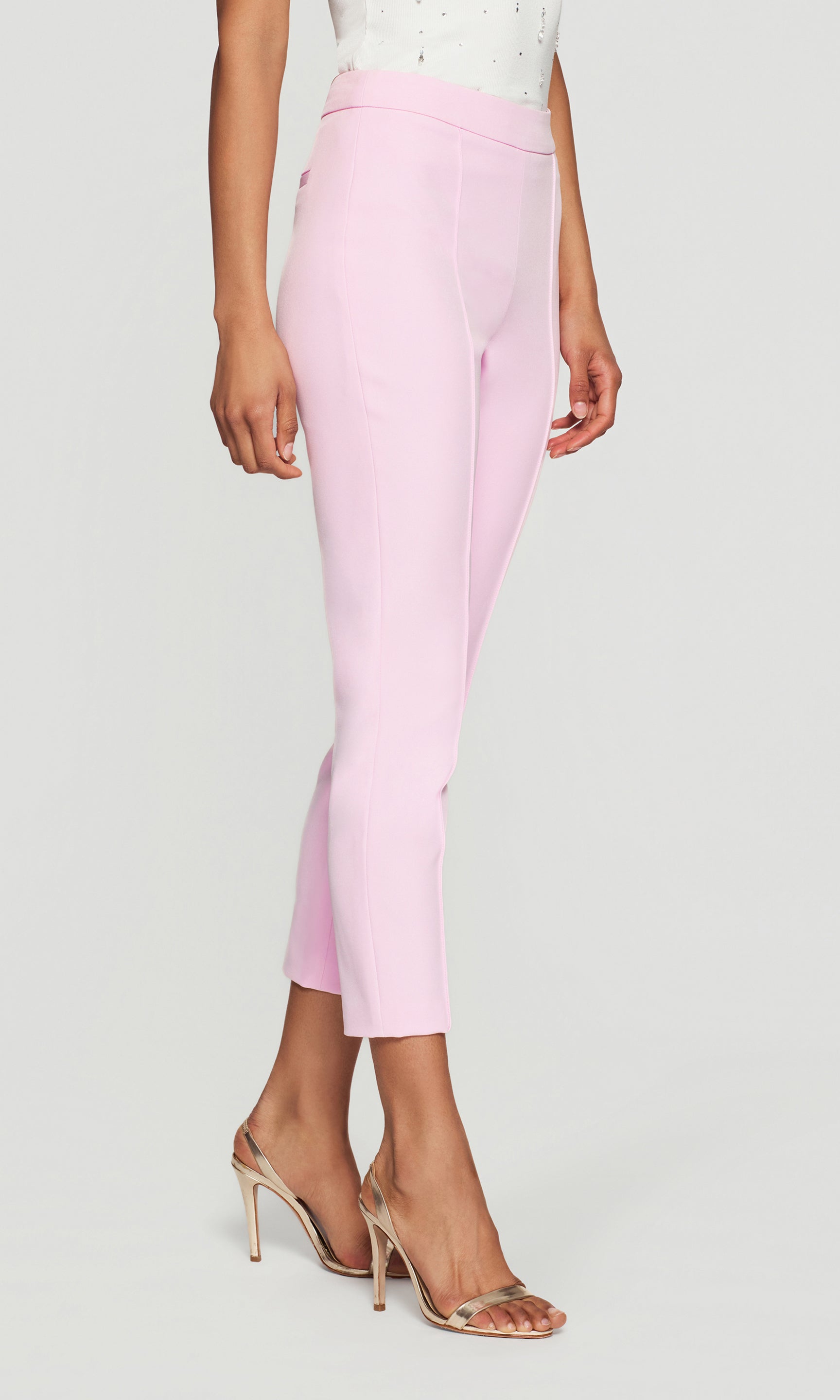 Side view of the model wearing the Lonny Crepe Pants in soft rose on a neutral background, showing the sleek side line, fitted waist, and tapered ankle length with heels.