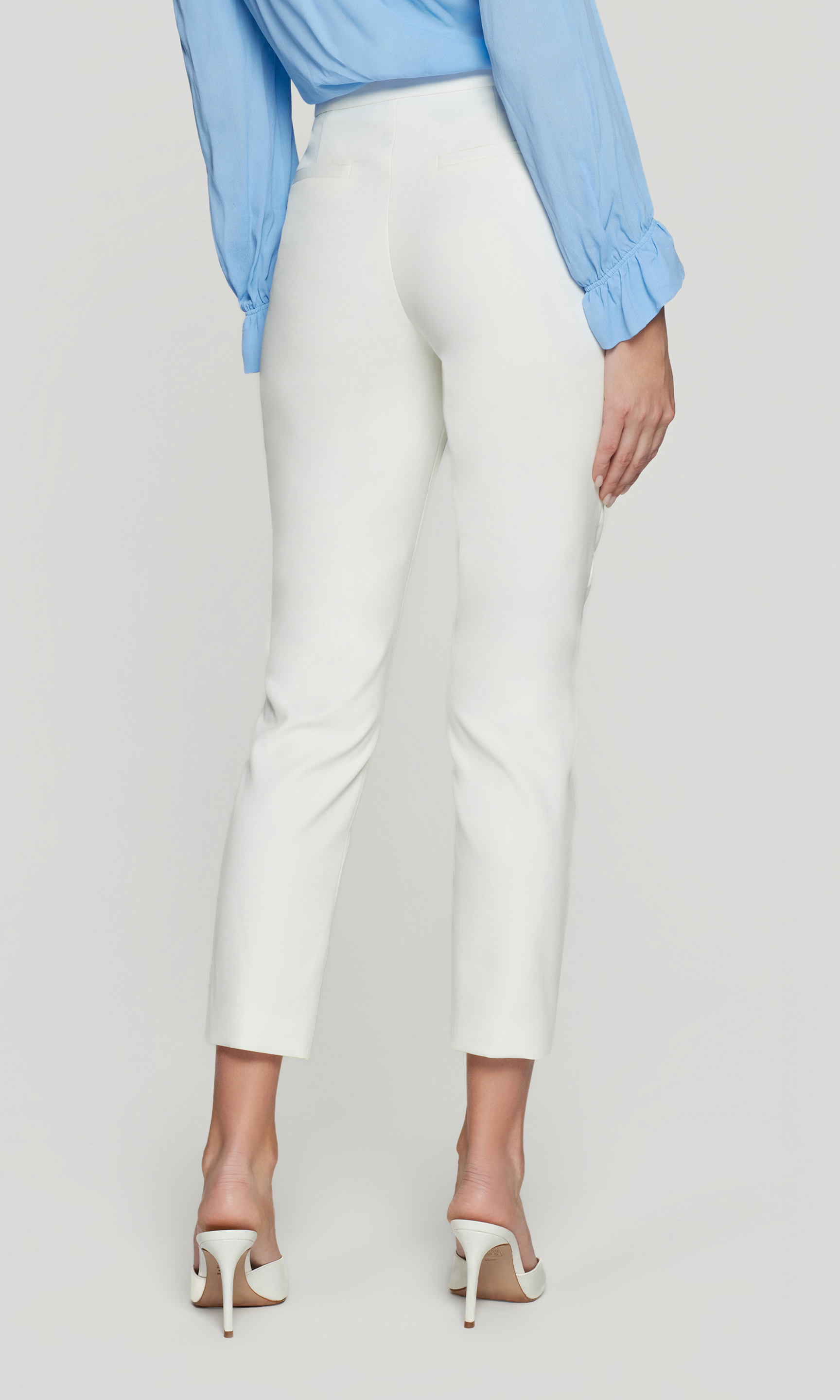 Back view of the model wearing the Lonny Crepe Pants in white, showing the smooth fit through the hips and the sleek tapered finish above the heel.