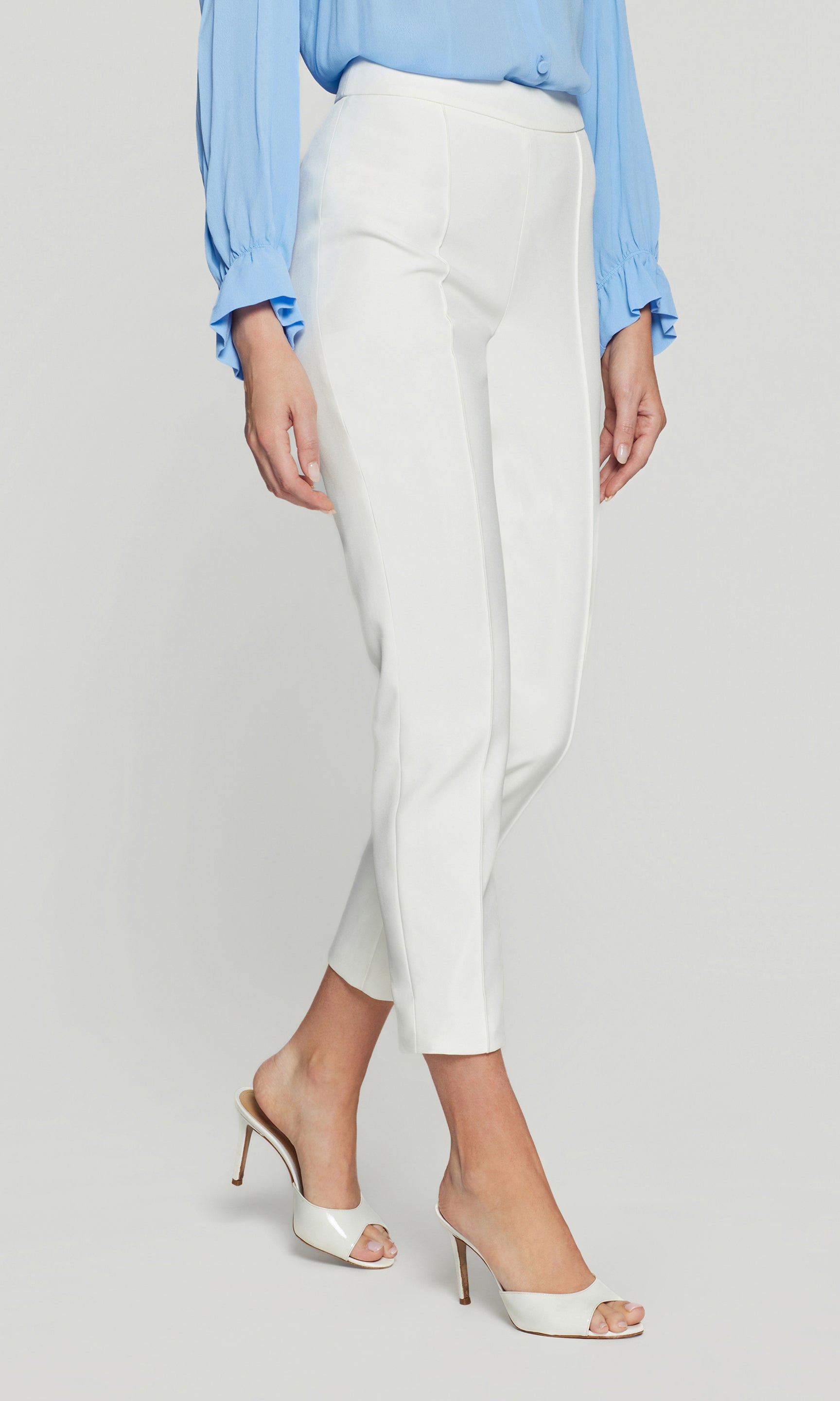 Side view of the model wearing the Lonny Crepe Pants in white, showing the sharp side line, flattering high waist, and polished ankle hem with heels.