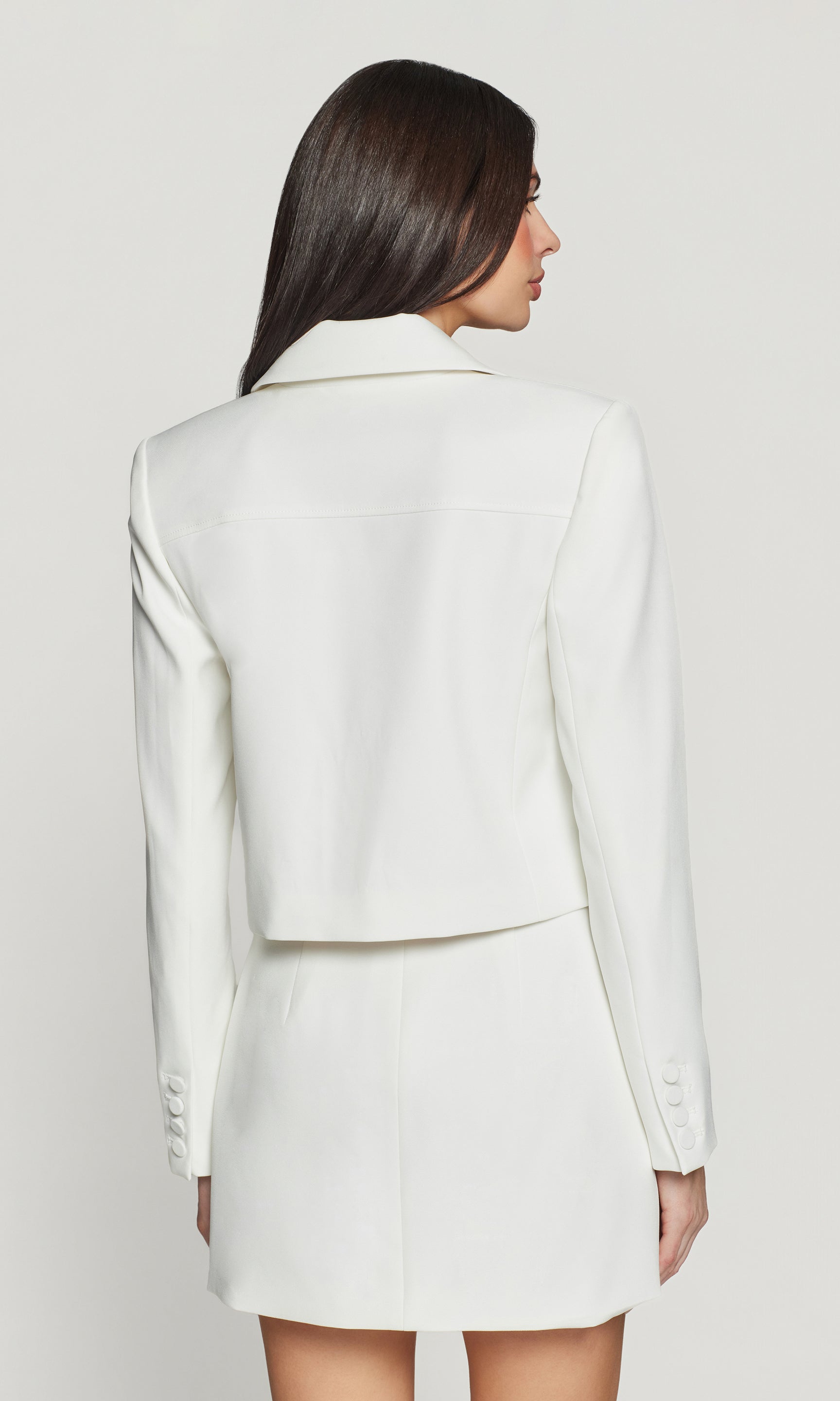 Woman wearing a white blazer and skirt set on a plain background