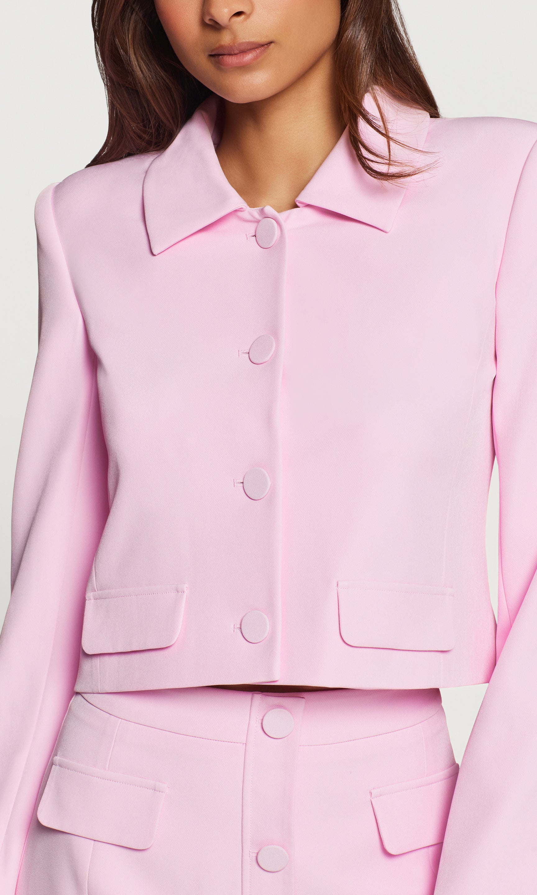In a studio close-up front view, the model wears the Luella Crepe Jacket in light pink, highlighting the clean tailoring and button details.