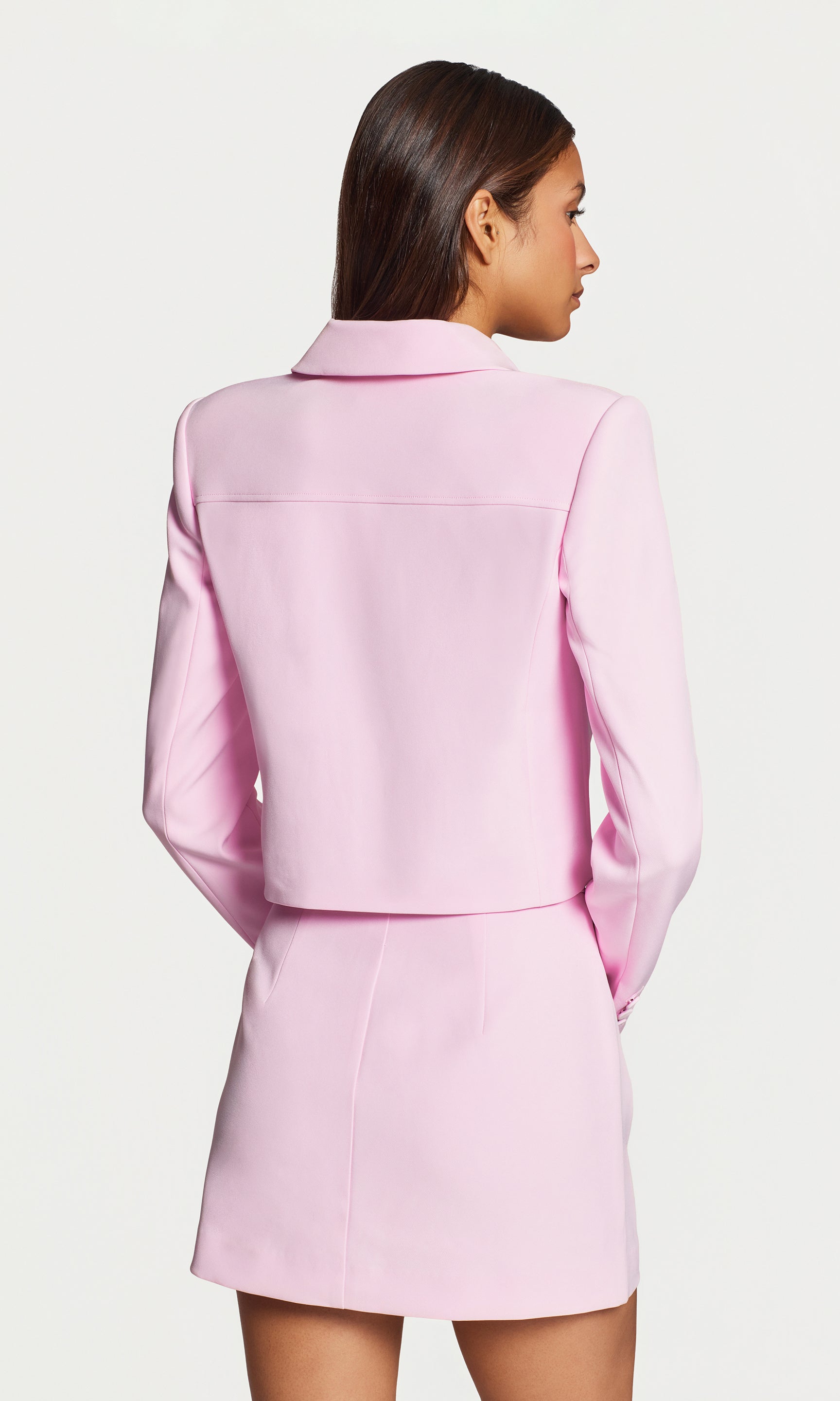 In a studio rear view, the model wears the Luella Crepe Jacket in light pink, showing the smooth back and structured shoulders.