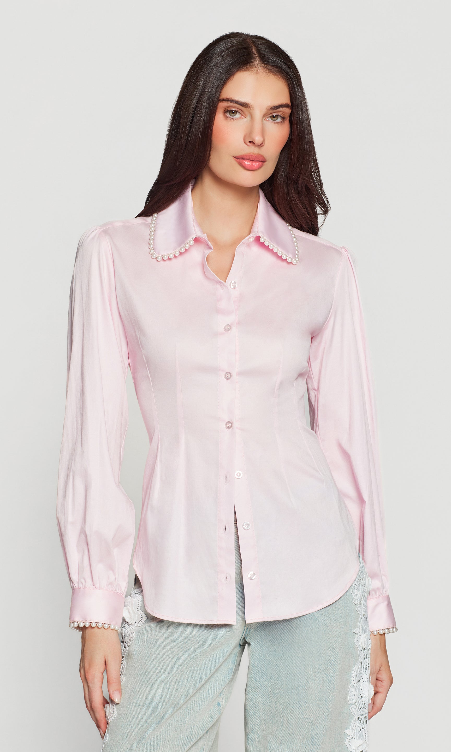 Woman wearing a light pink top with pearl embellishments on a white background