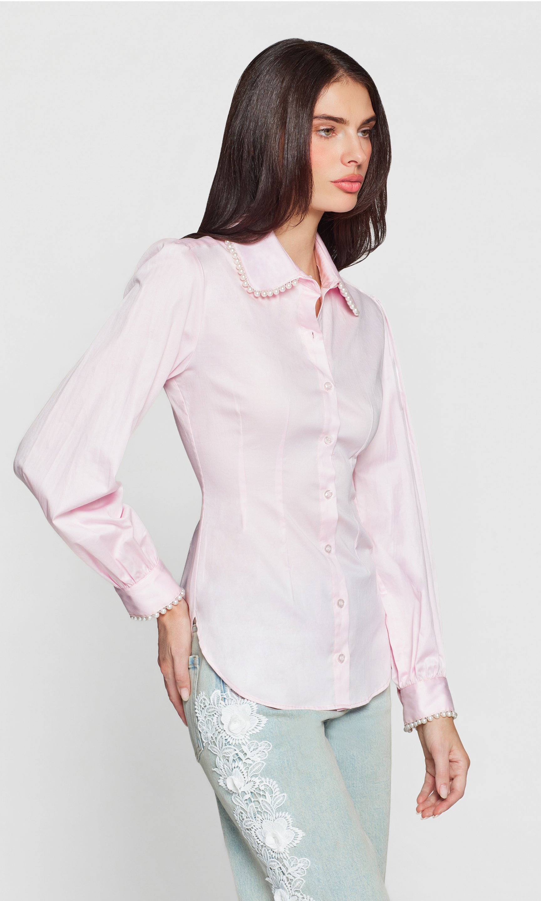 Side view of woman wearing a light pink top with pearl embellishments on a white background