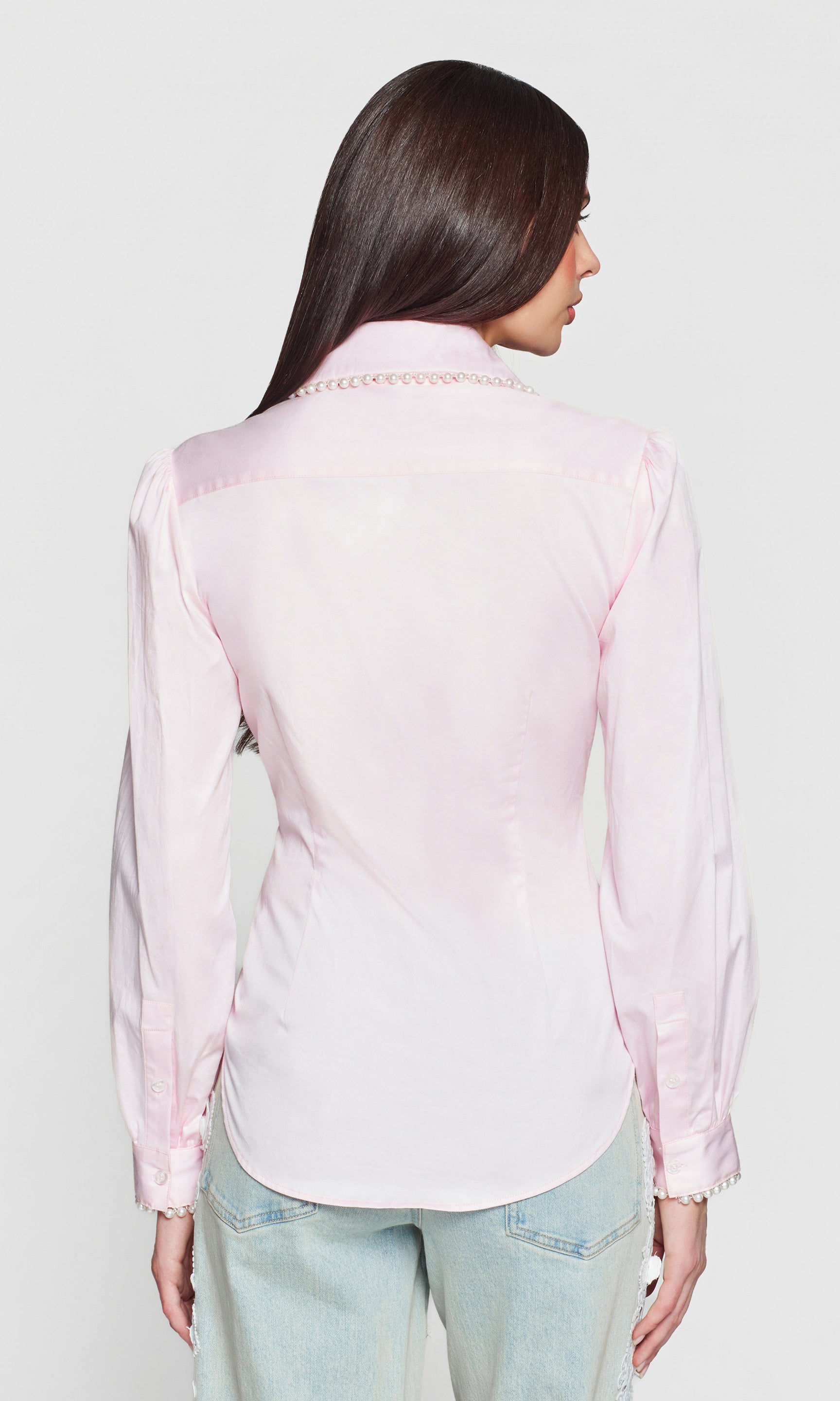 Back view of woman wearing a light pink top with pearl embellishments on a white background
