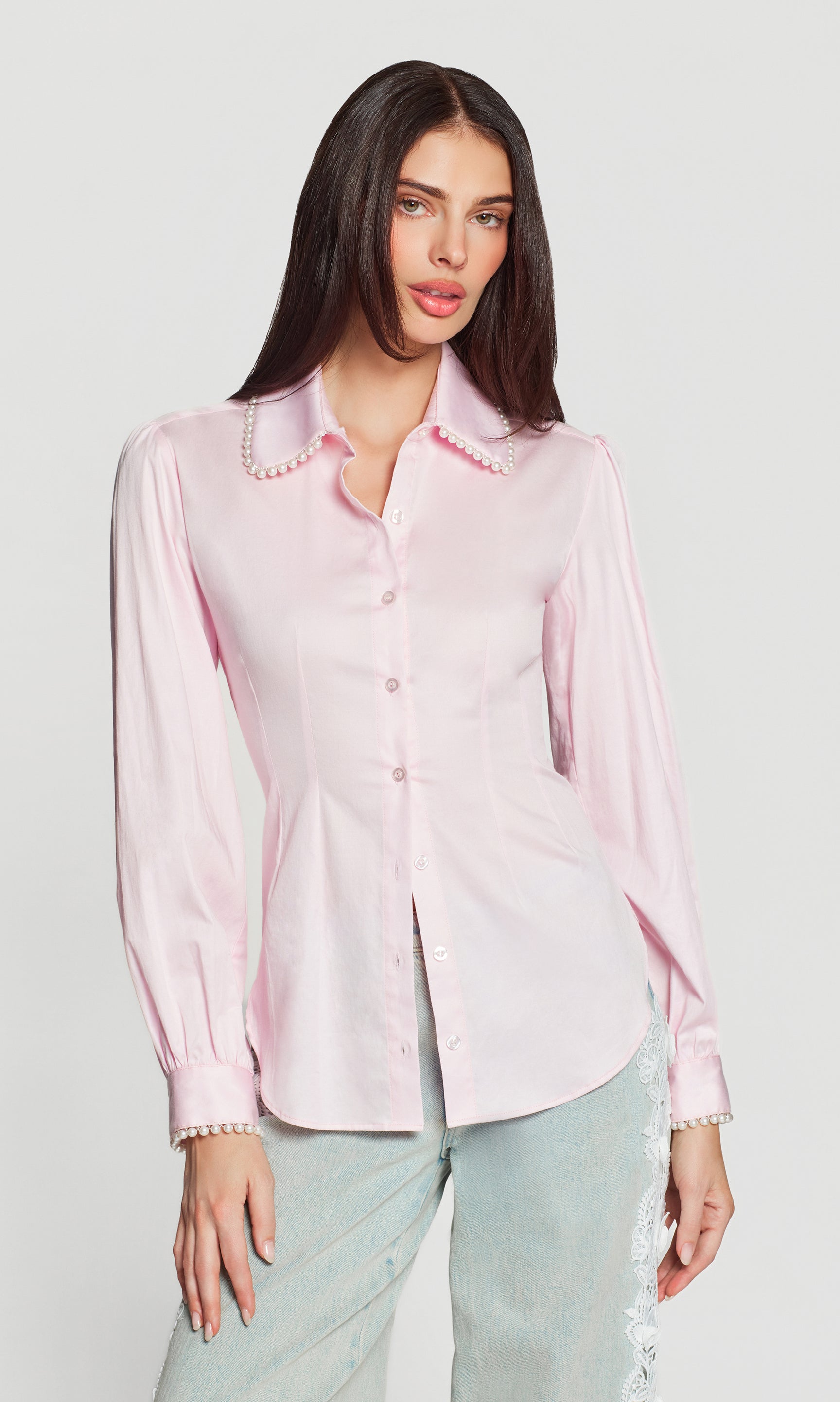 Woman wearing a light pink blouse with pearl trim on a white background
