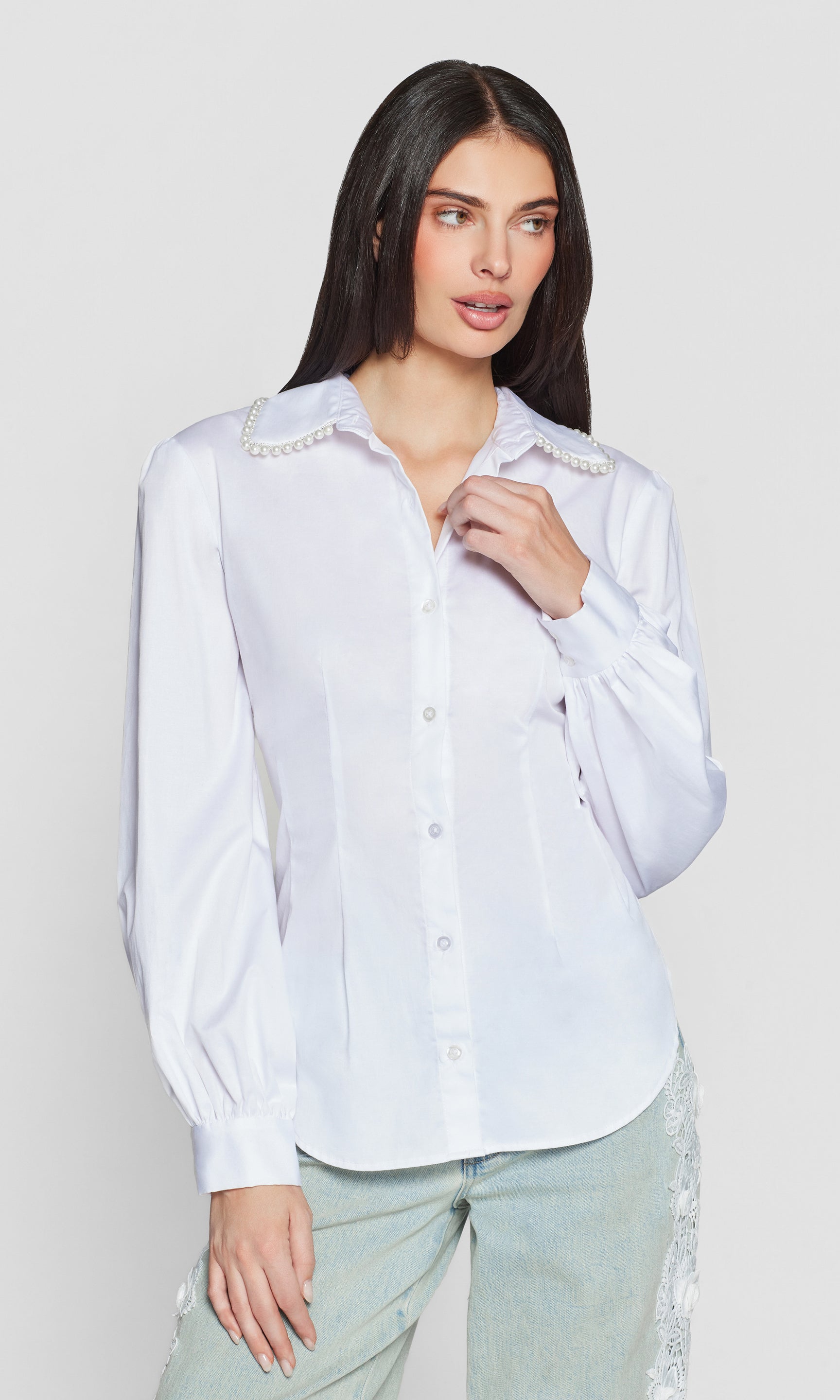 Woman wearing a white blouse with pearl details on a plain background