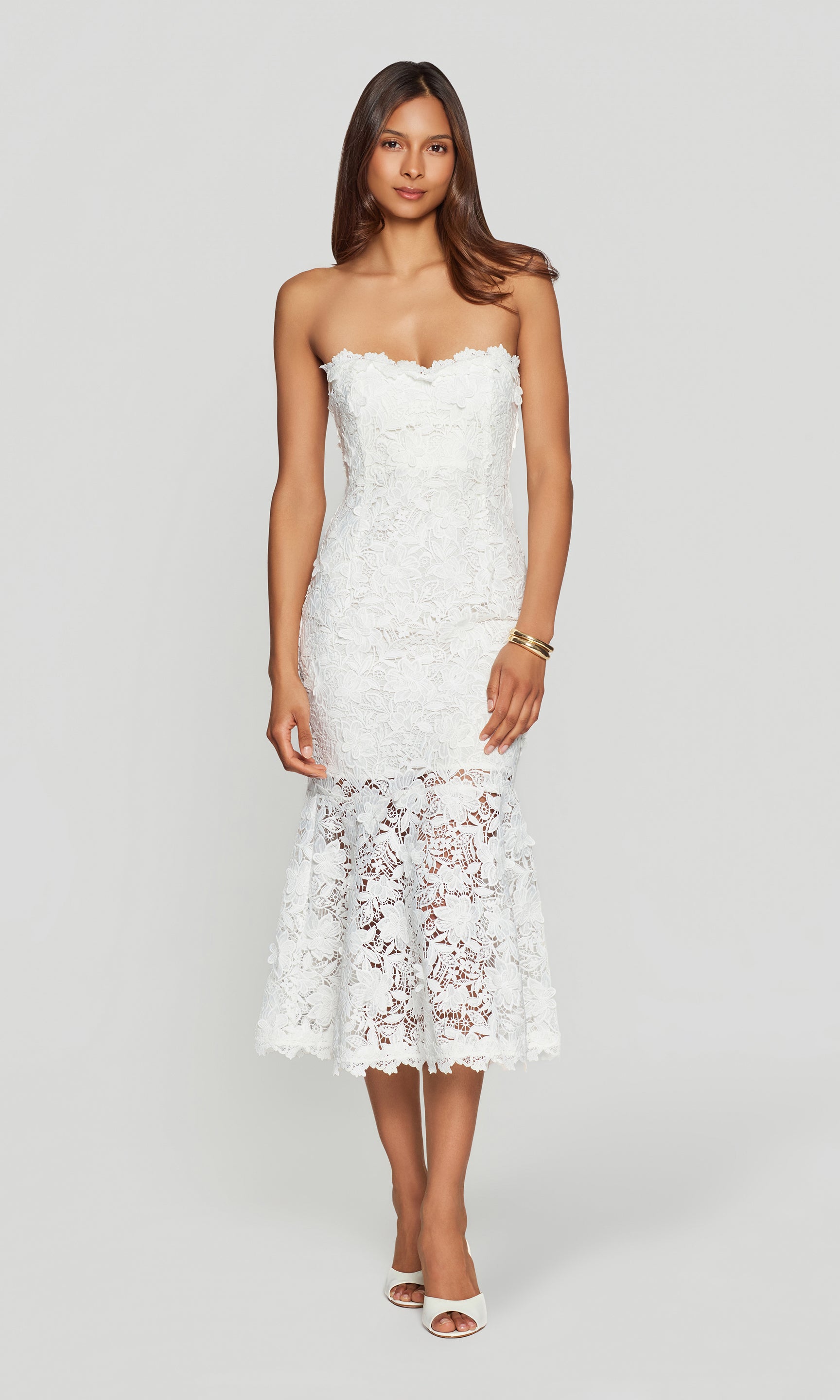 Woman wearing a strapless white lace dress on a plain background