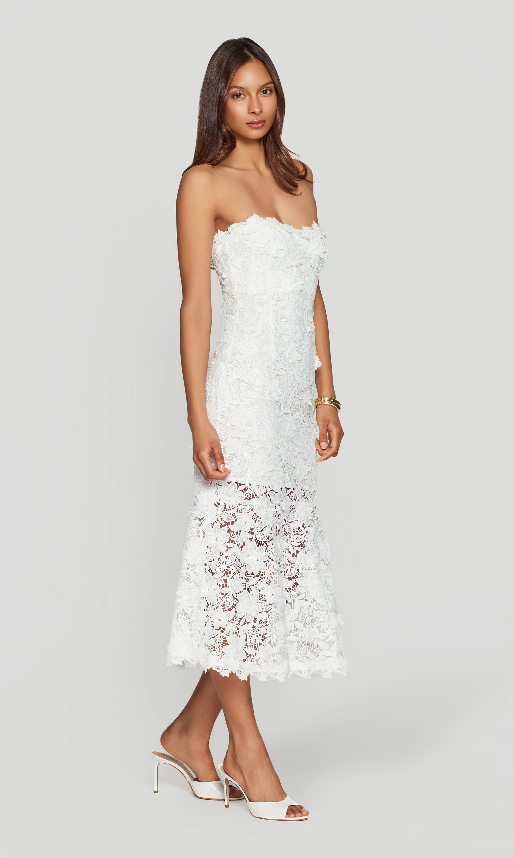 Side view of woman wearing a white strapless lace dress on a plain background