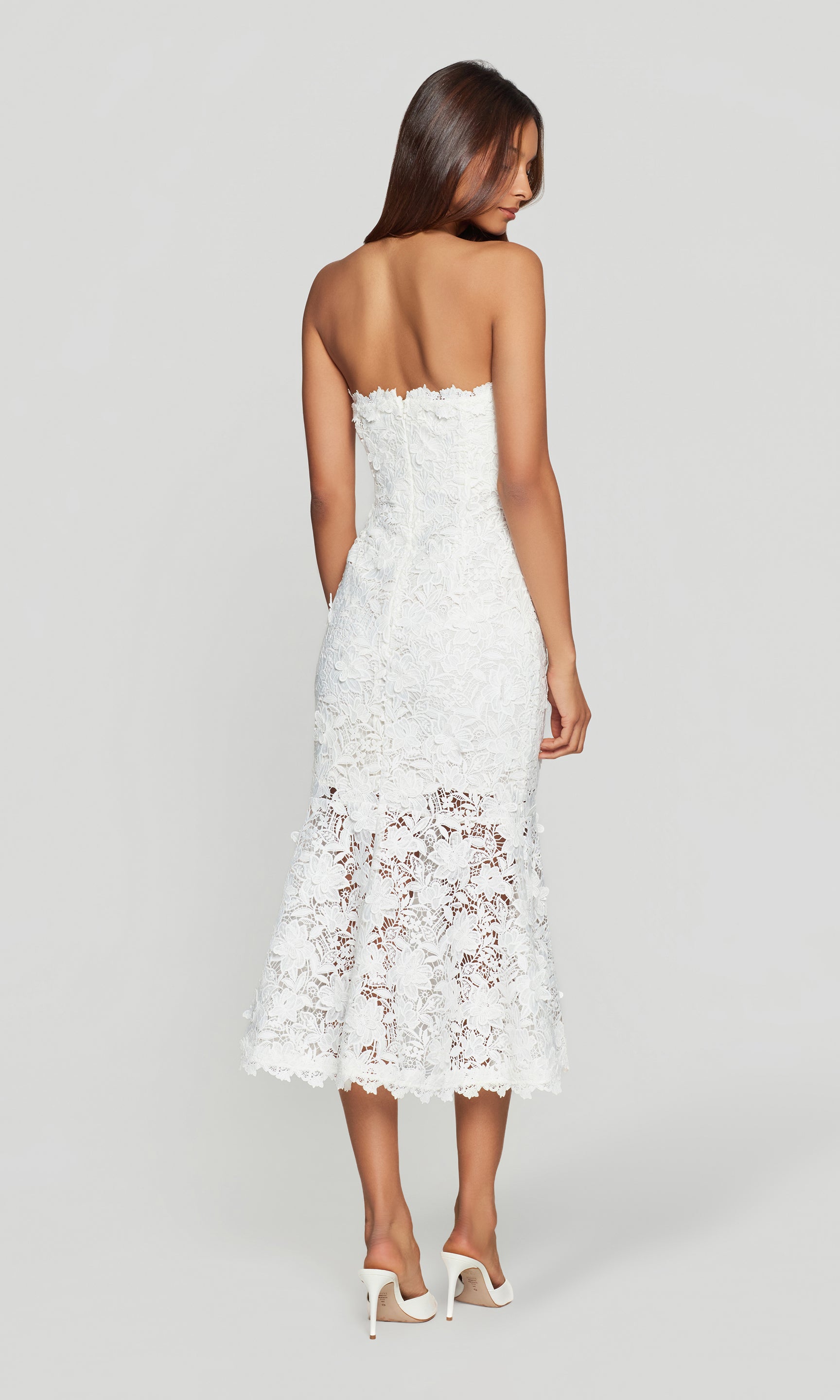 Back view of woman wearing a white lace strapless dress on a light gray background