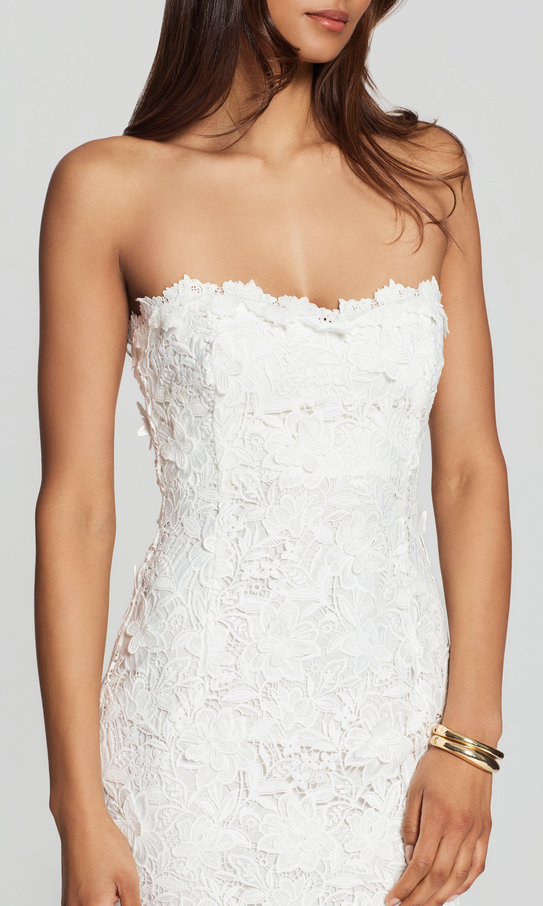 Close-up of white strapless lace dress worn by a model on a plain background