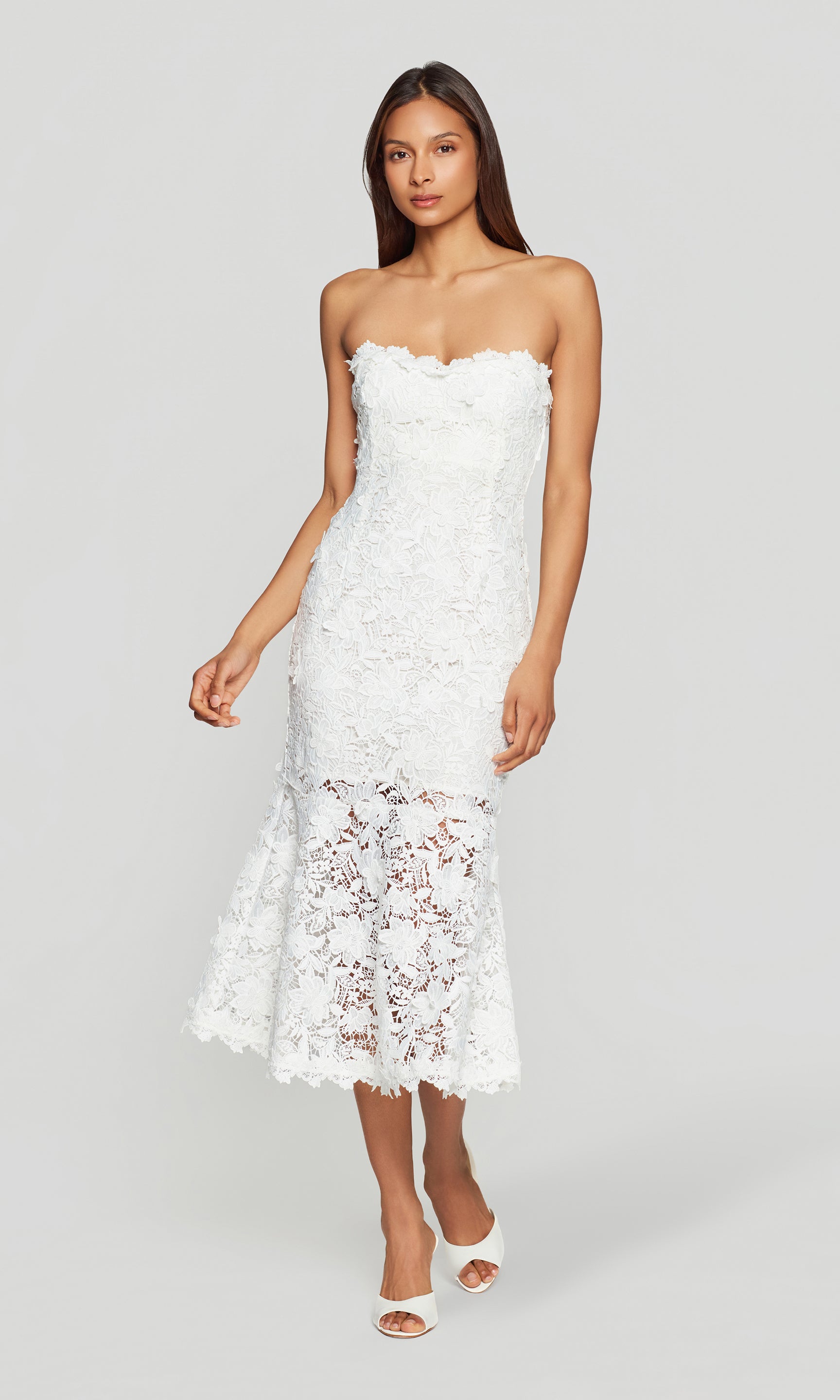 Woman wearing a white strapless lace dress on a plain background