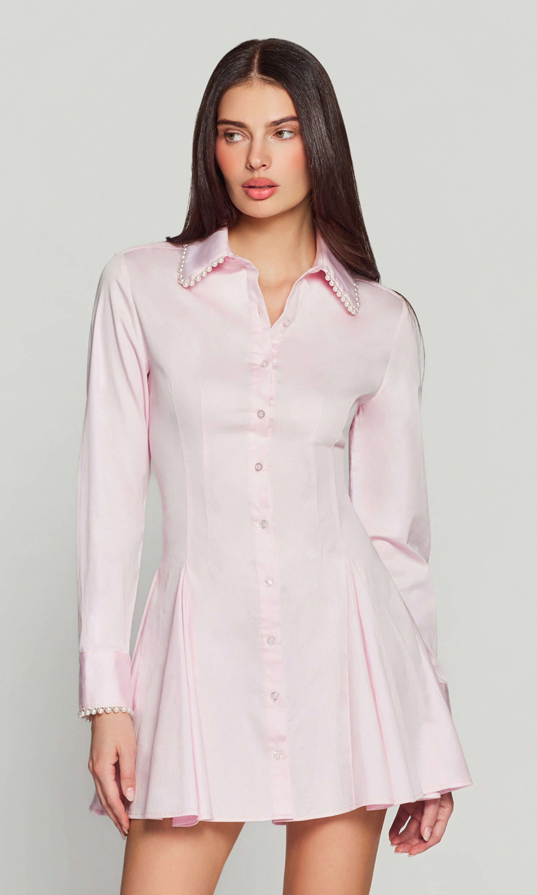 Woman wearing a light pink dress with pearl trim on a plain background