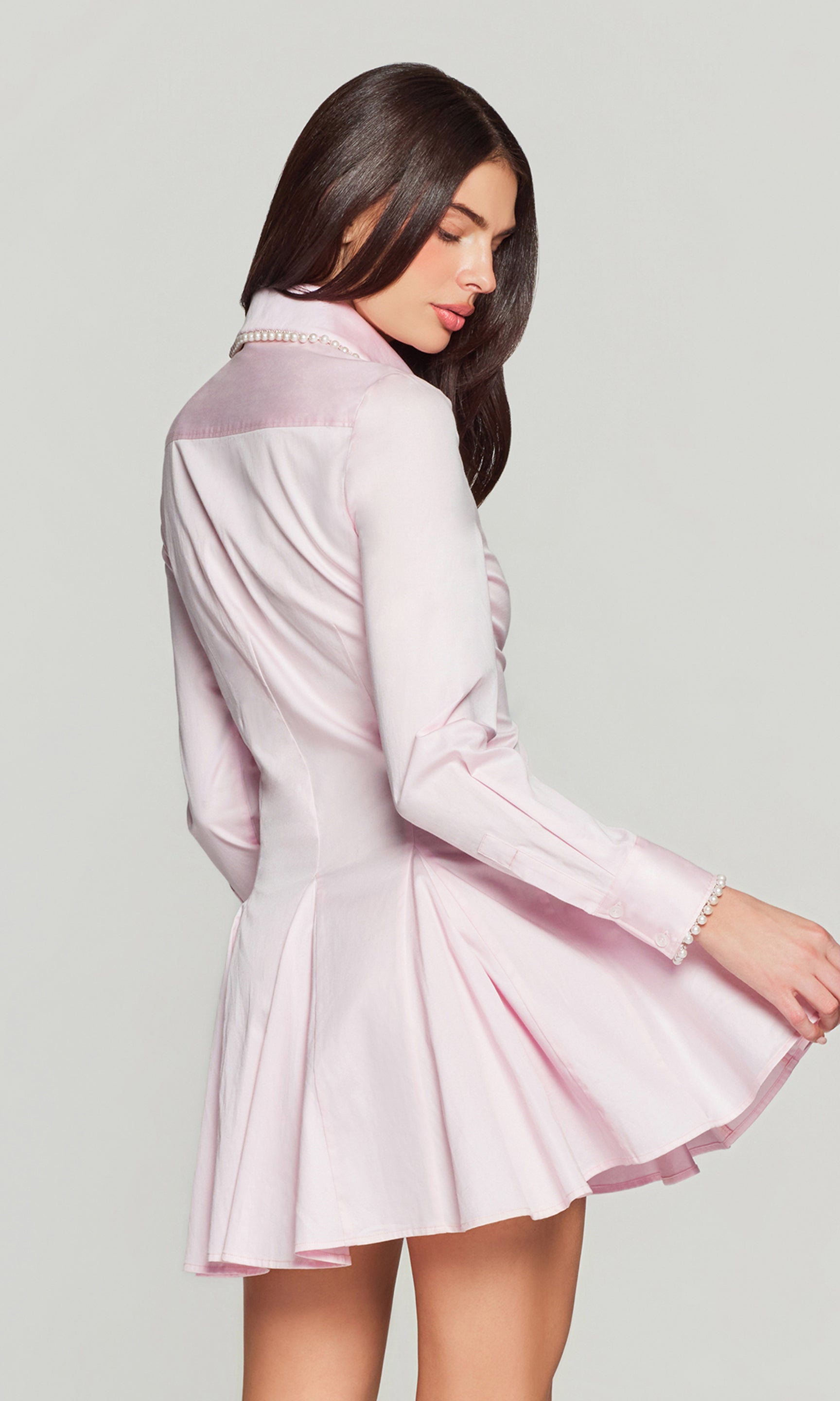 Back view of woman wearing a light pink dress with long sleeves on a plain background
