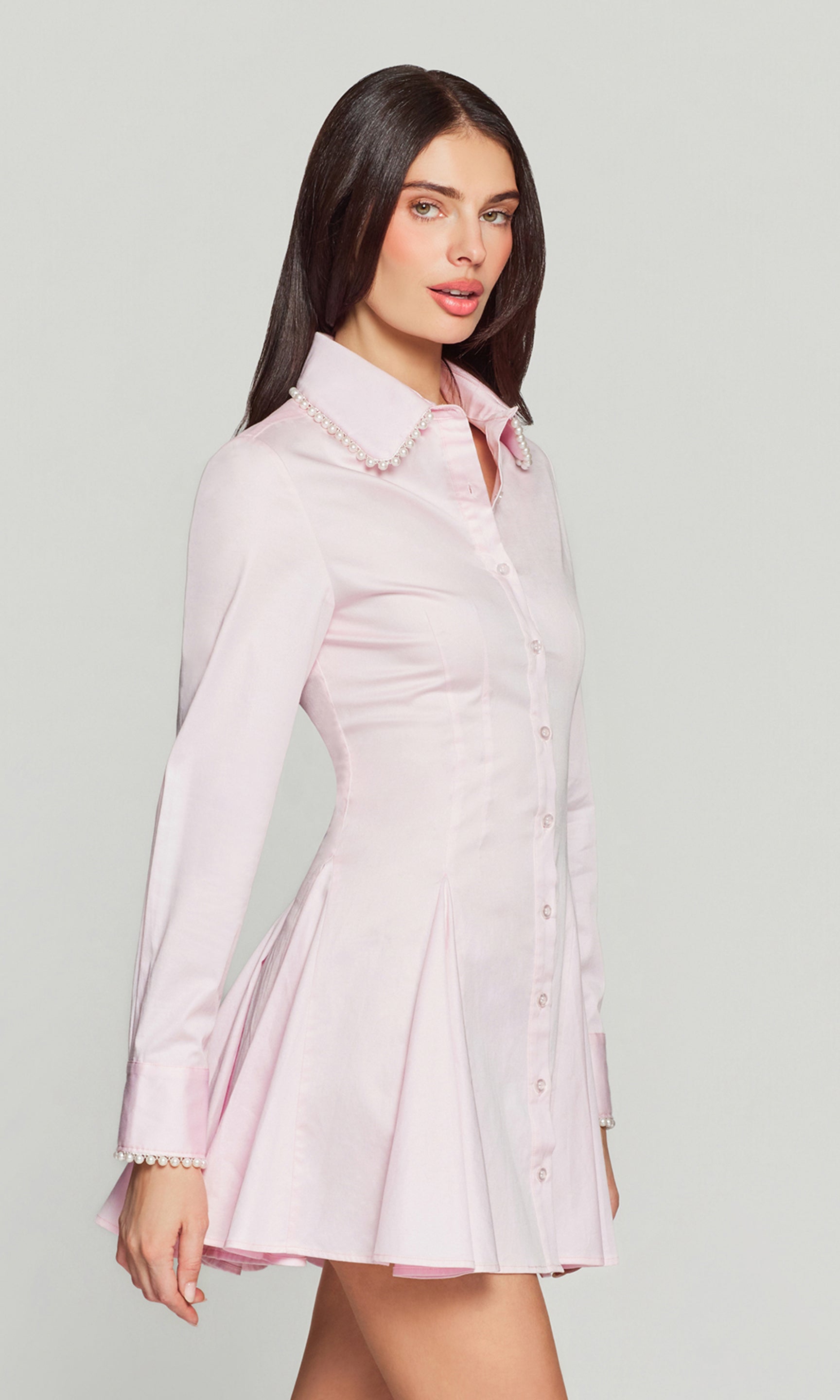 Side view of woman wearing a light pink dress with pearl trim on a gray background