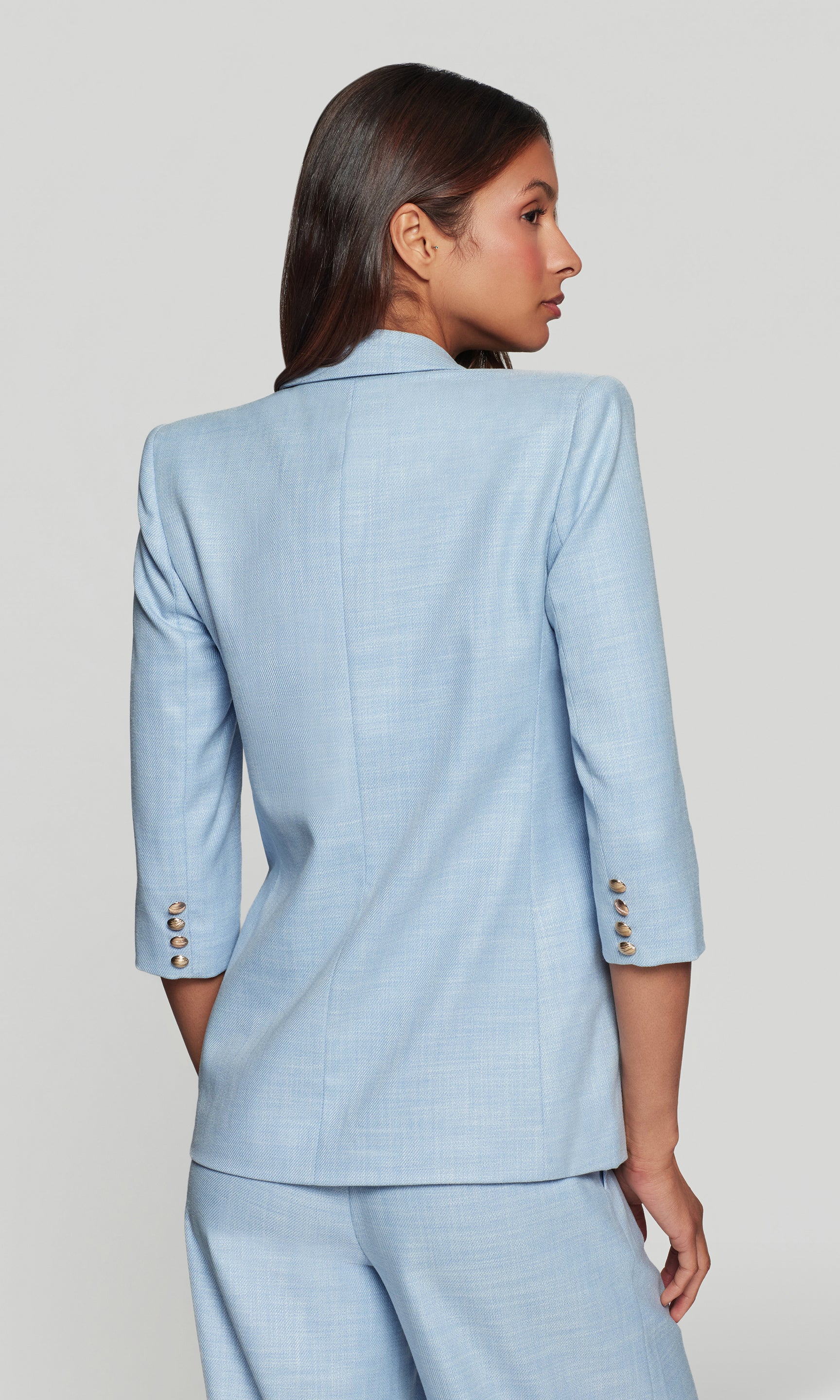 Back view of woman wearing a light blue suit with a plain background