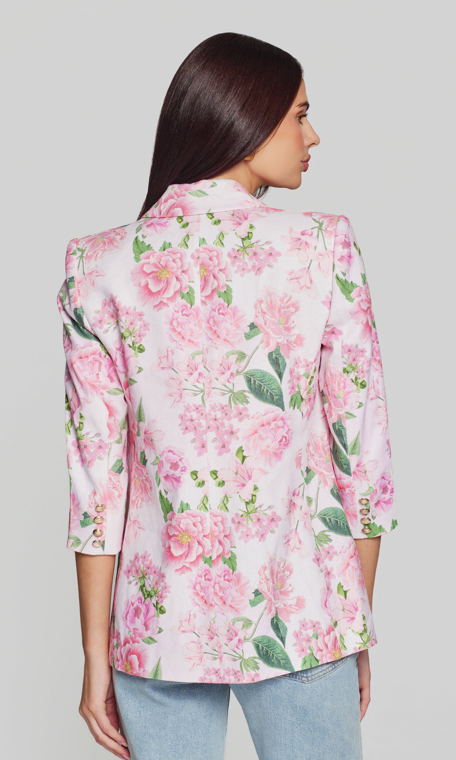 Back view of woman wearing a floral blazer with pink flowers and green leaves on a plain background