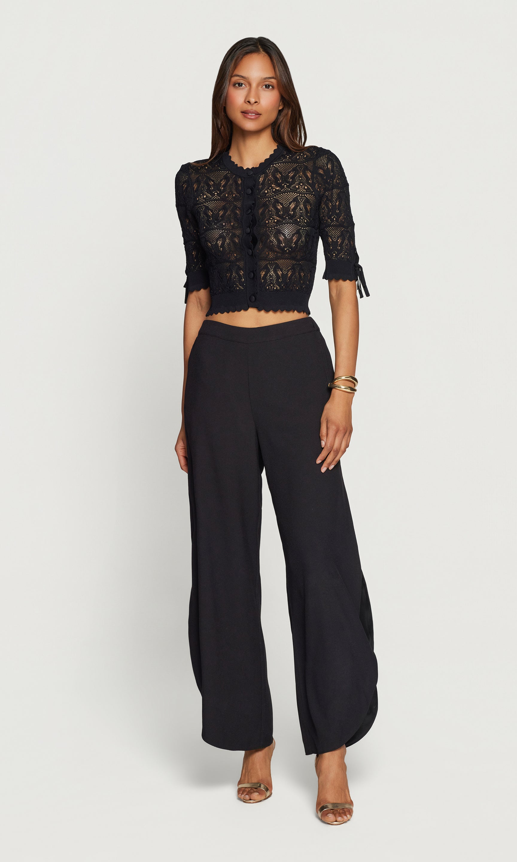 Woman wearing a black lace cardigan and wide-leg pants on a white background