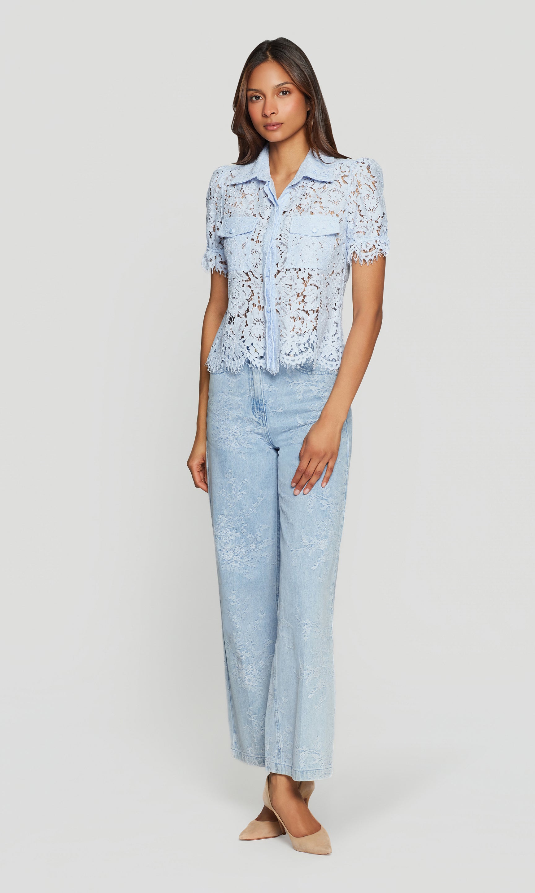 Full body image of woman wearing a light blue lace top and jeans on a white background