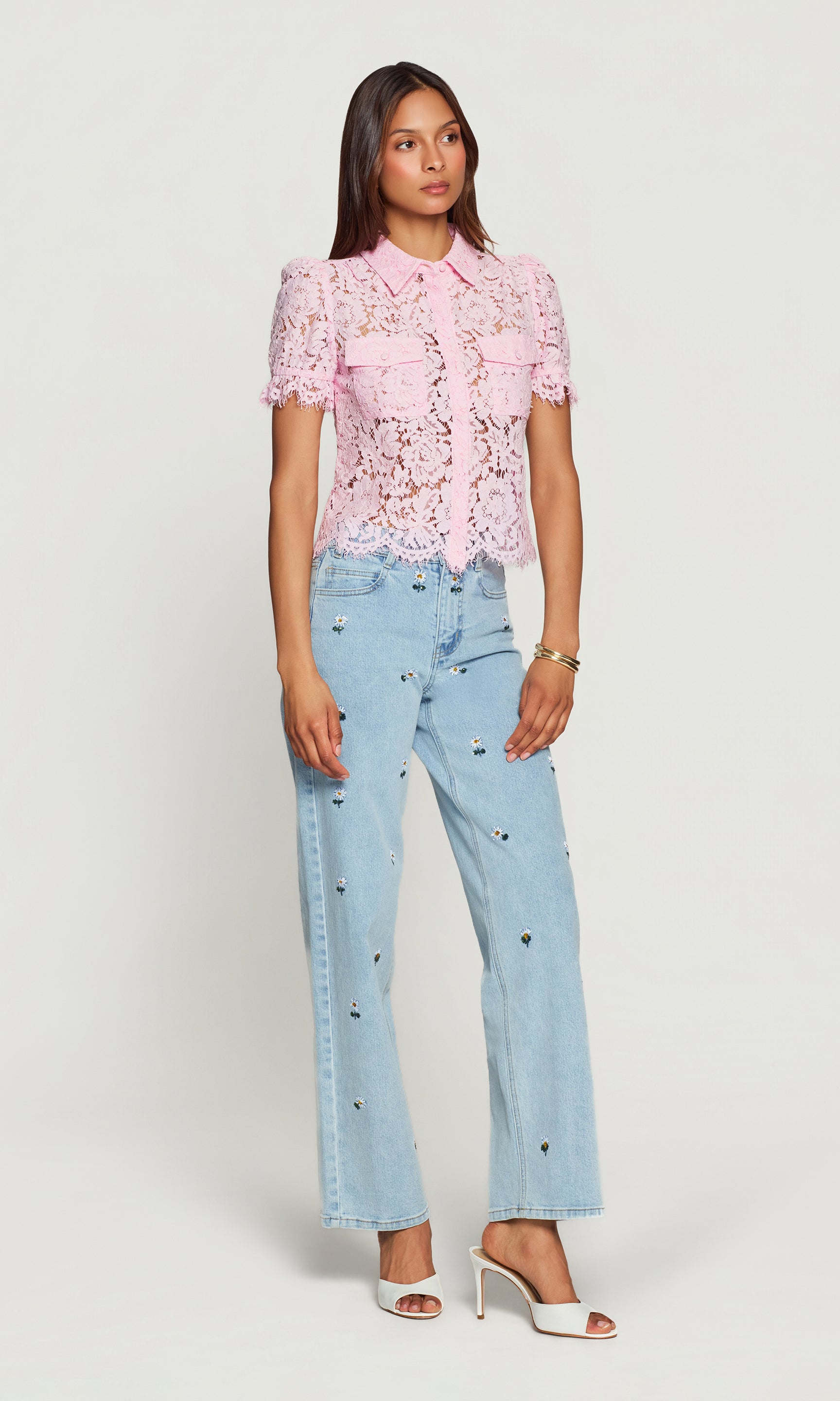 Woman wearing a pink lace blouse and light blue jeans on a white background