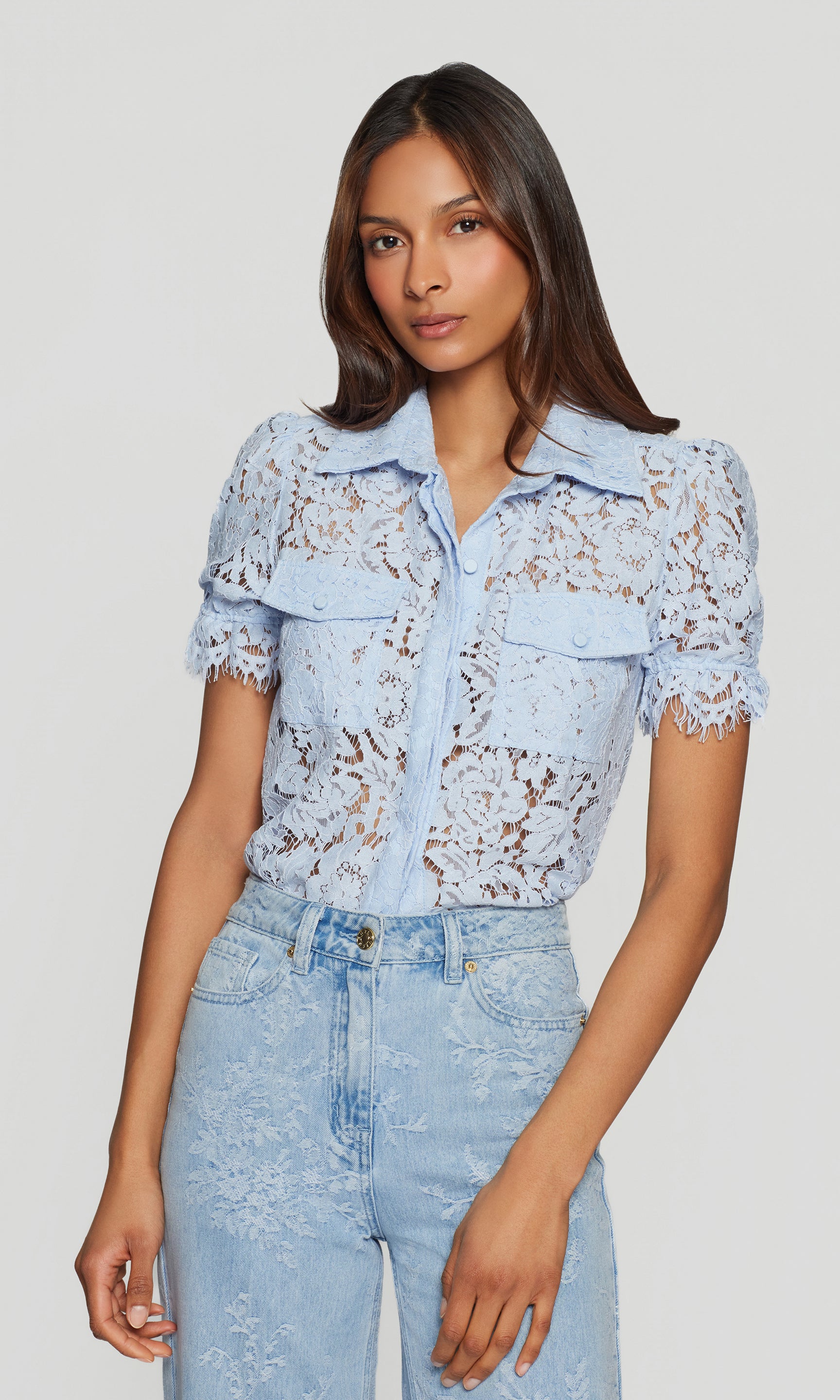 Woman wearing a light blue lace top and jeans on a plain background