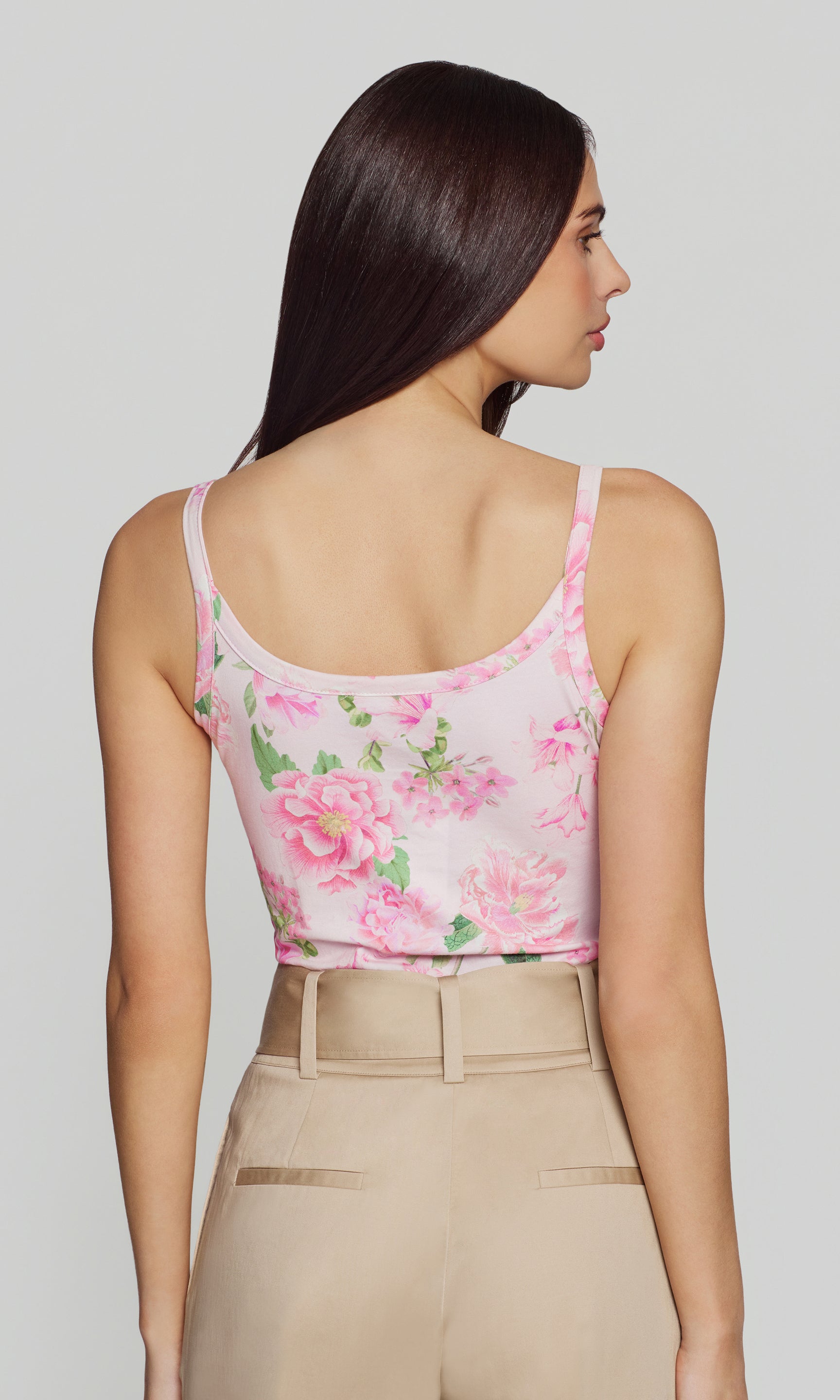 Back view of woman wearing a floral pink top and beige pants on a plain background