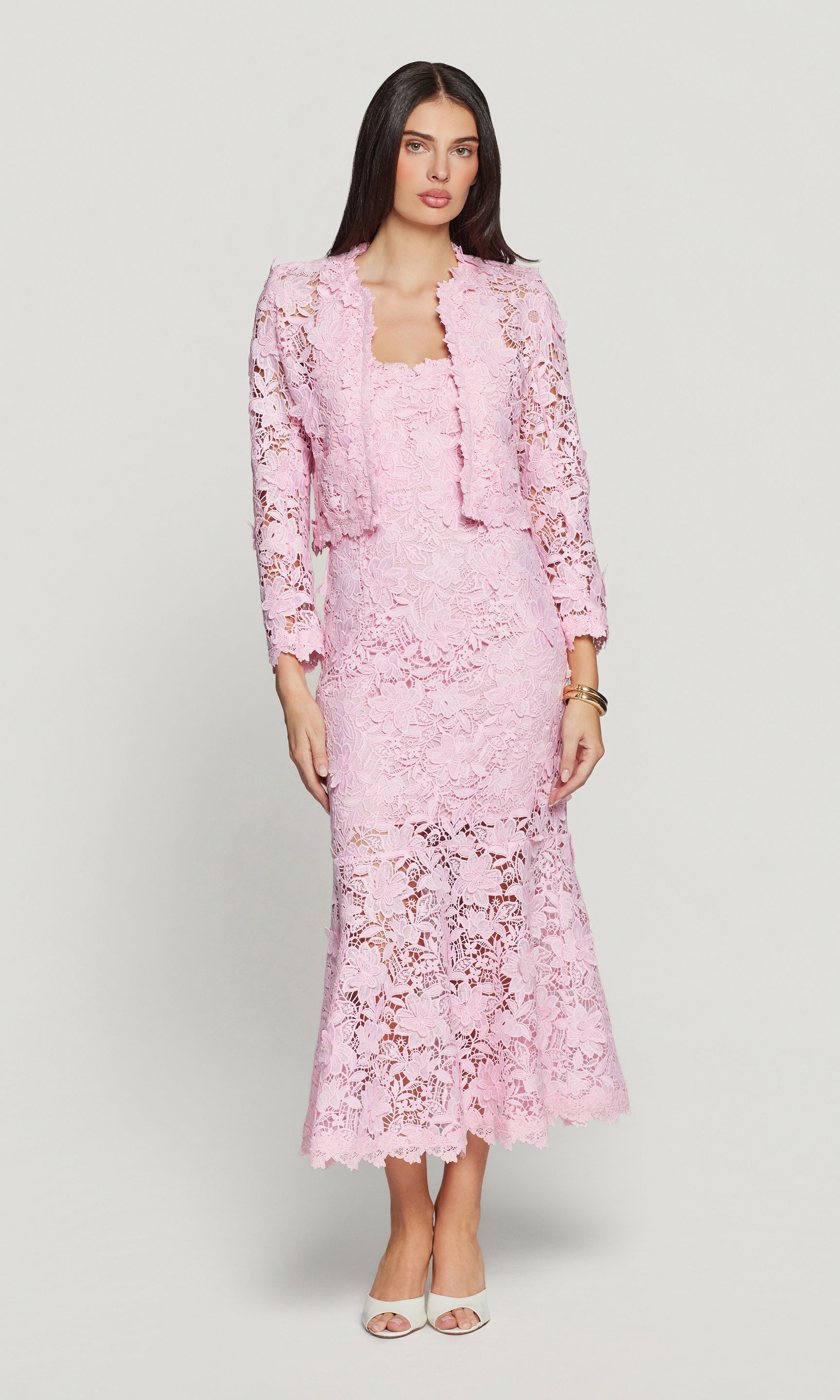 Woman wearing a pink lace dress with matching jacket on a white background