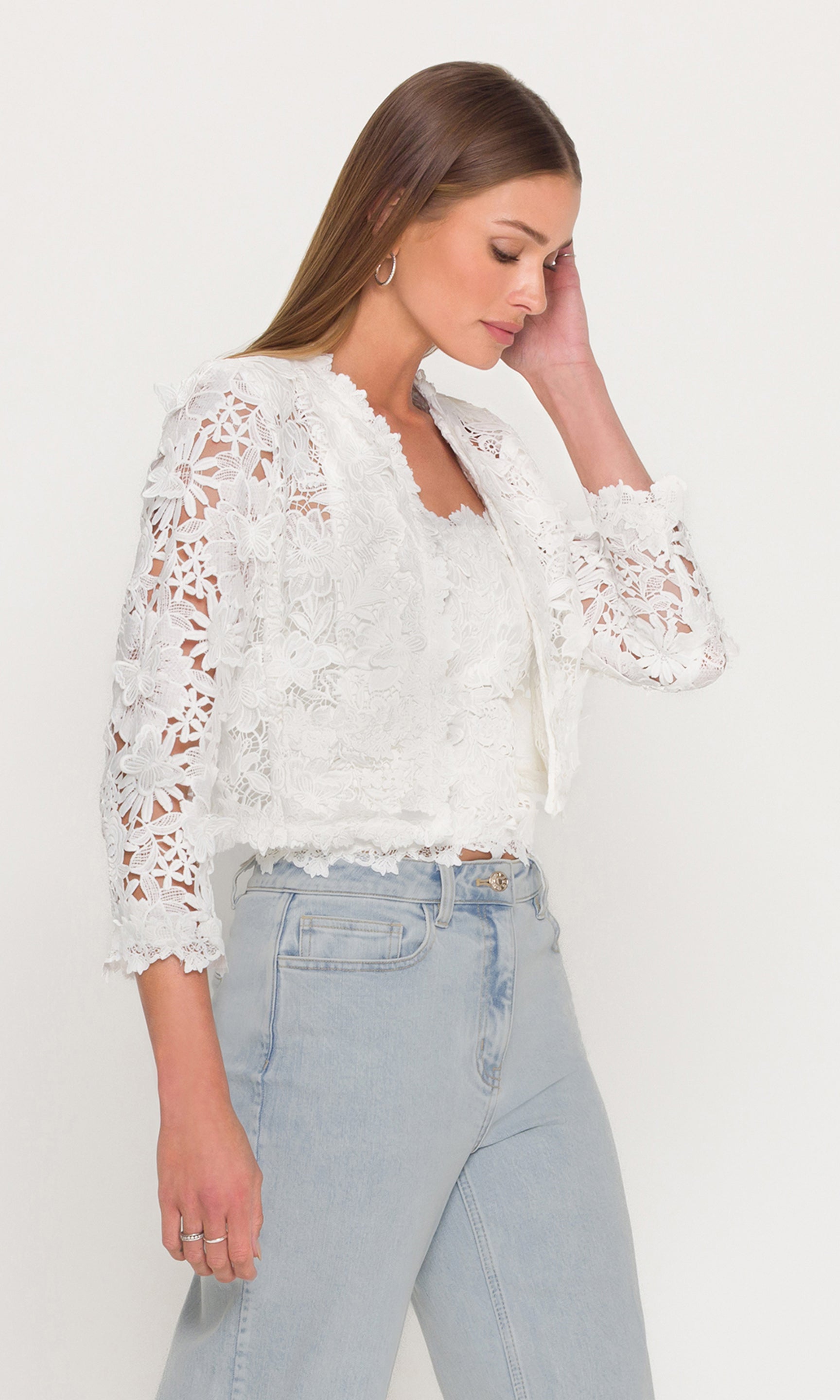Side view of woman wearing a white lace jacket and light blue jeans on a white background