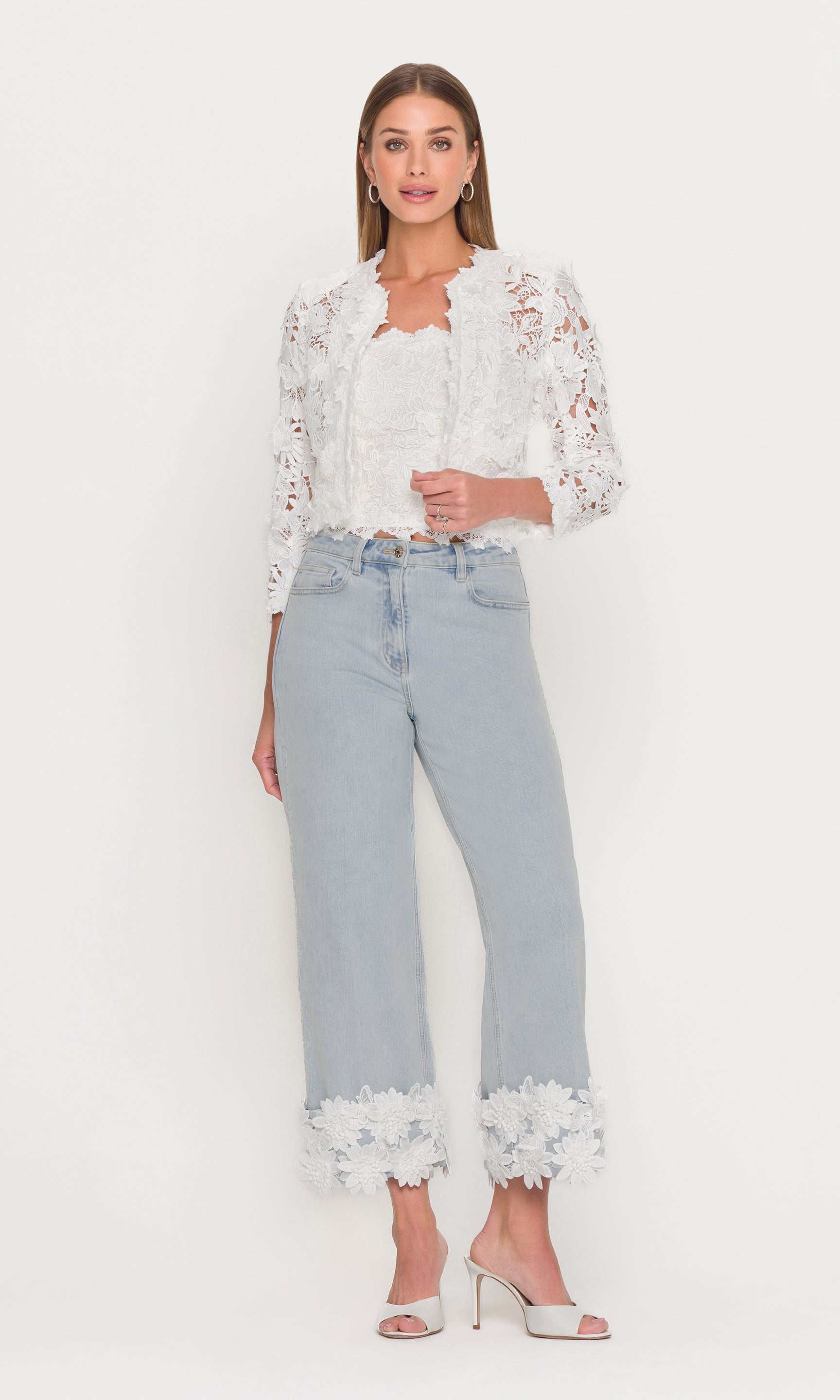 Woman wearing a white lace jacket and top with light blue jeans with white lace trim on a white background