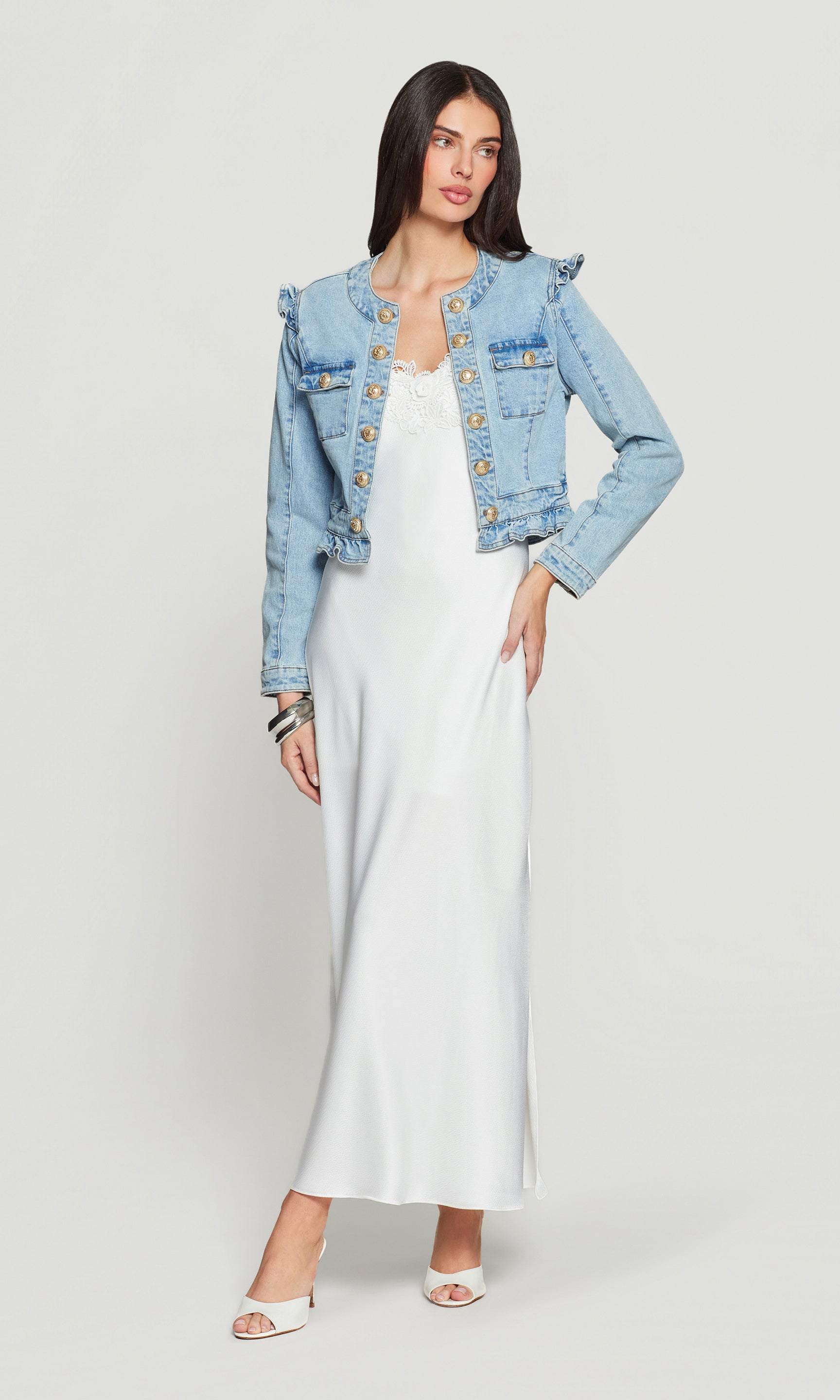 Woman wearing a light blue denim jacket over a white dress on a white background