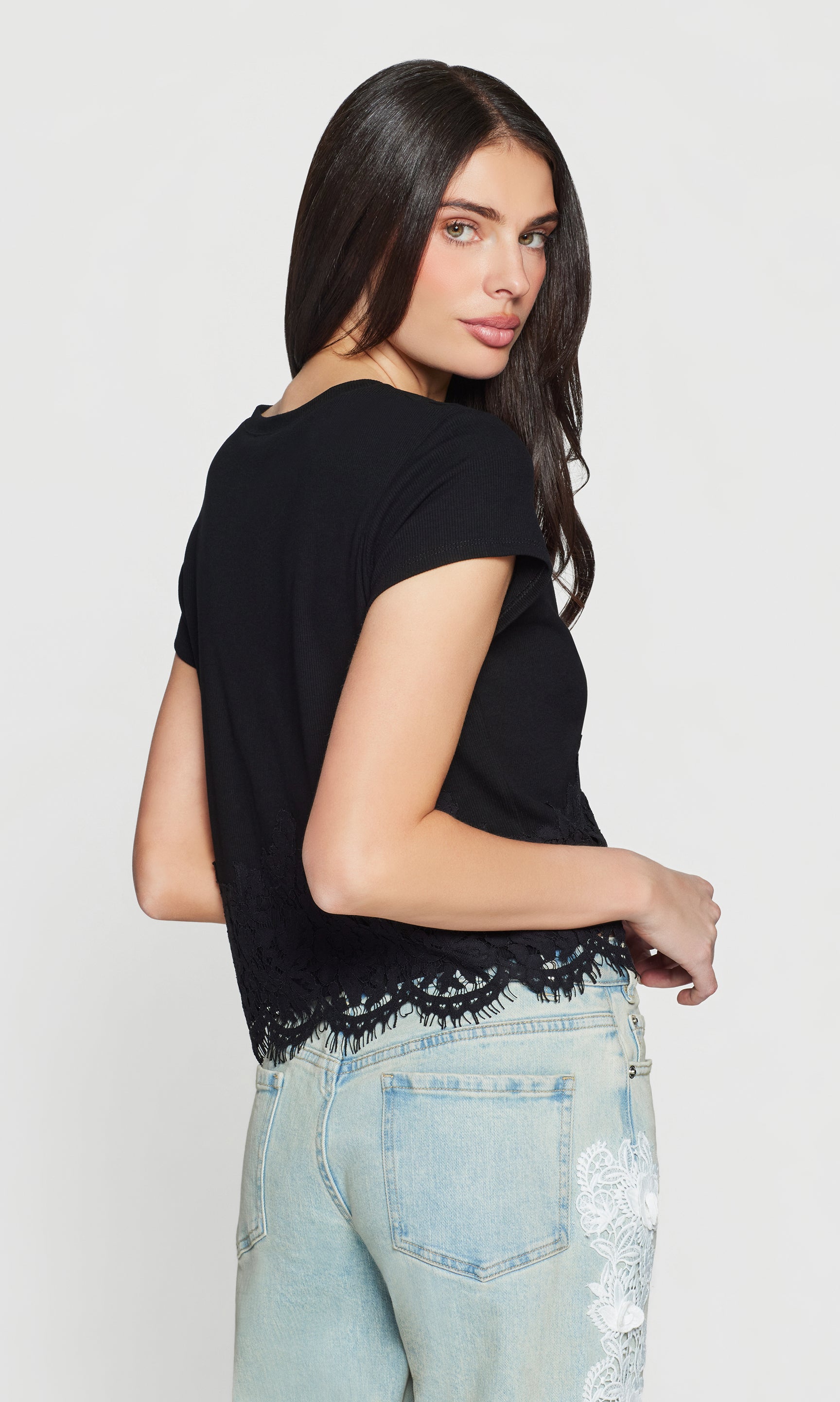 Side view of woman wearing a black top with lace details and light blue jeans on a white background