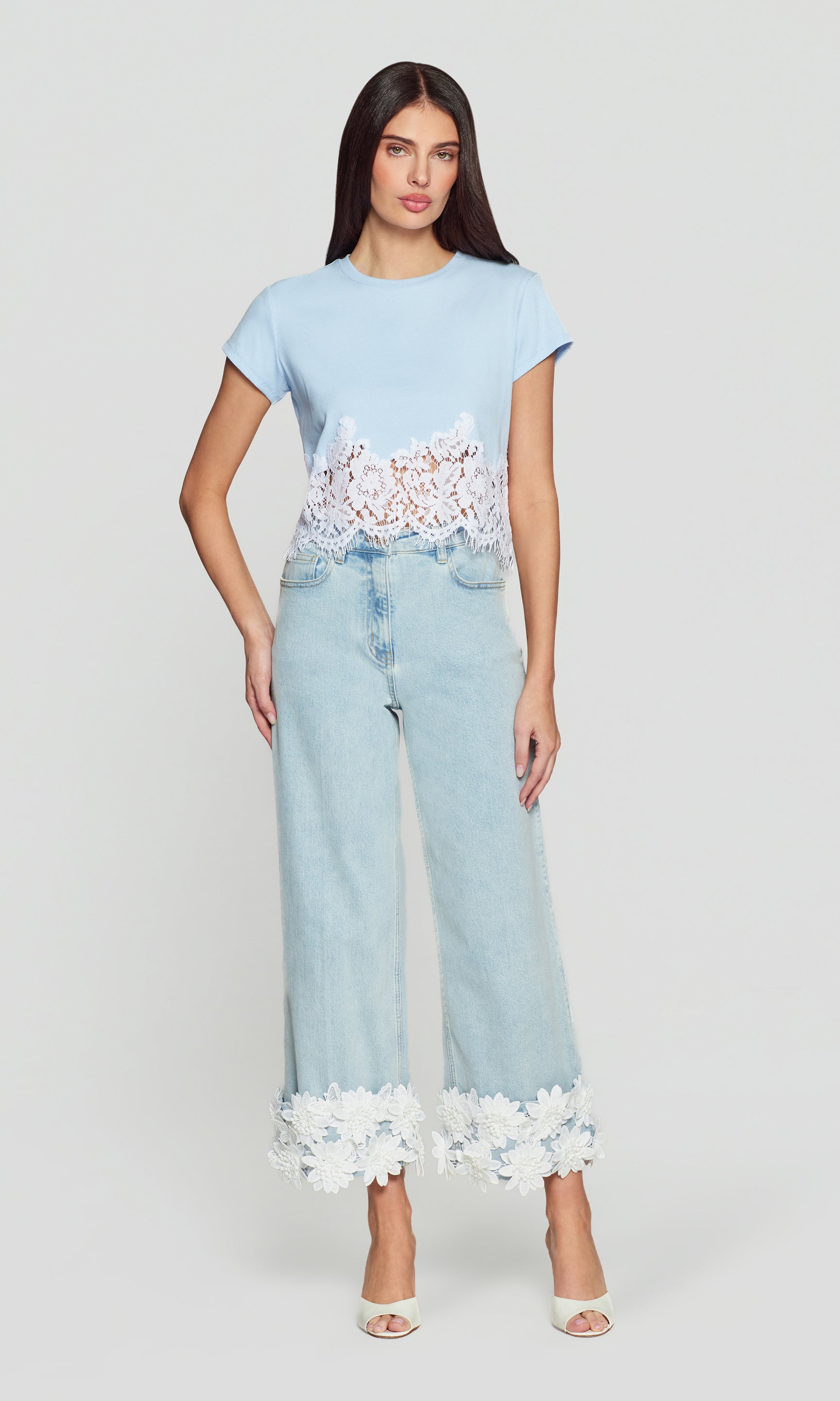 Woman wearing a light blue top and jeans with lace details on a white background