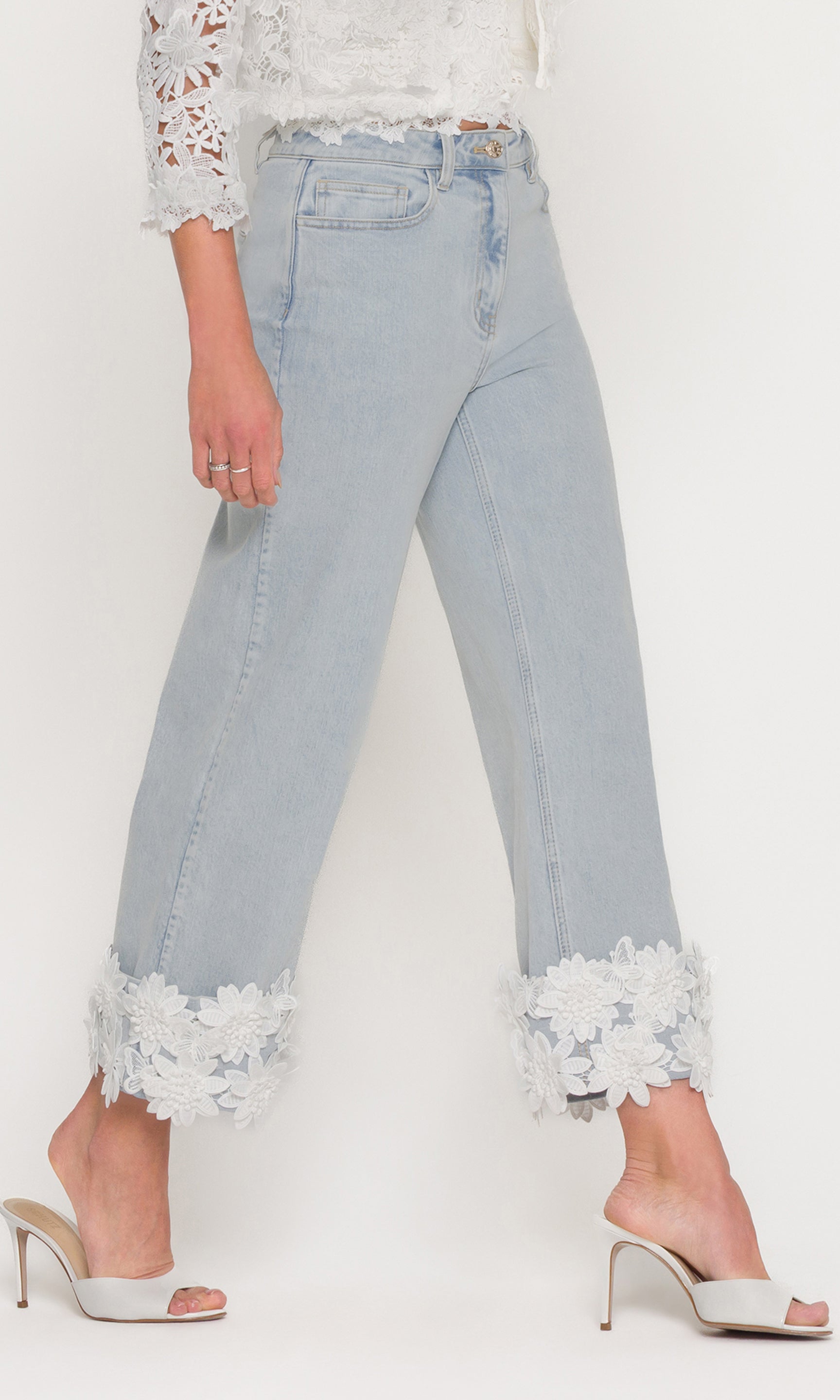 In a three-quarter front view, the model wears the Paloma Lace Combo Jeans in light wash denim, focusing on the cropped wide-leg cut and bold lace cuffs at the hem.