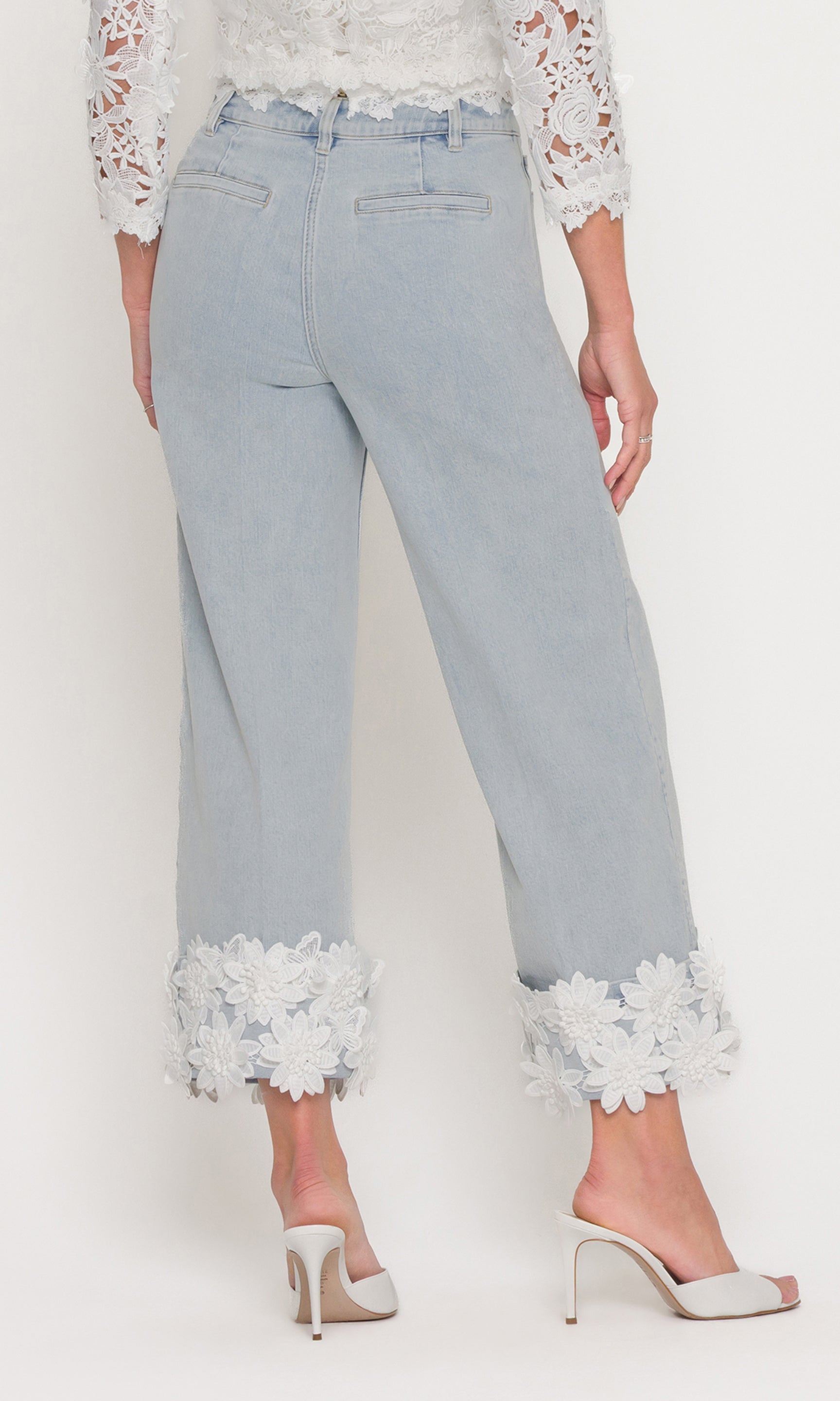 In a rear view, the model wears the Paloma Lace Combo Jeans in light wash denim, showing the back fit and the lace cuff finish from behind.