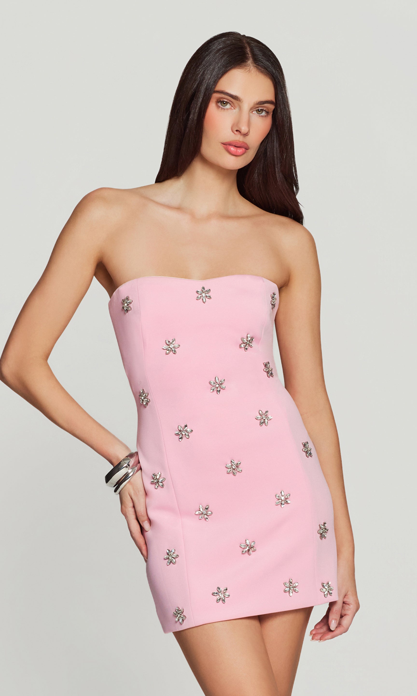 Woman wearing a pink strapless dress with floral crystal embellishments on a plain background