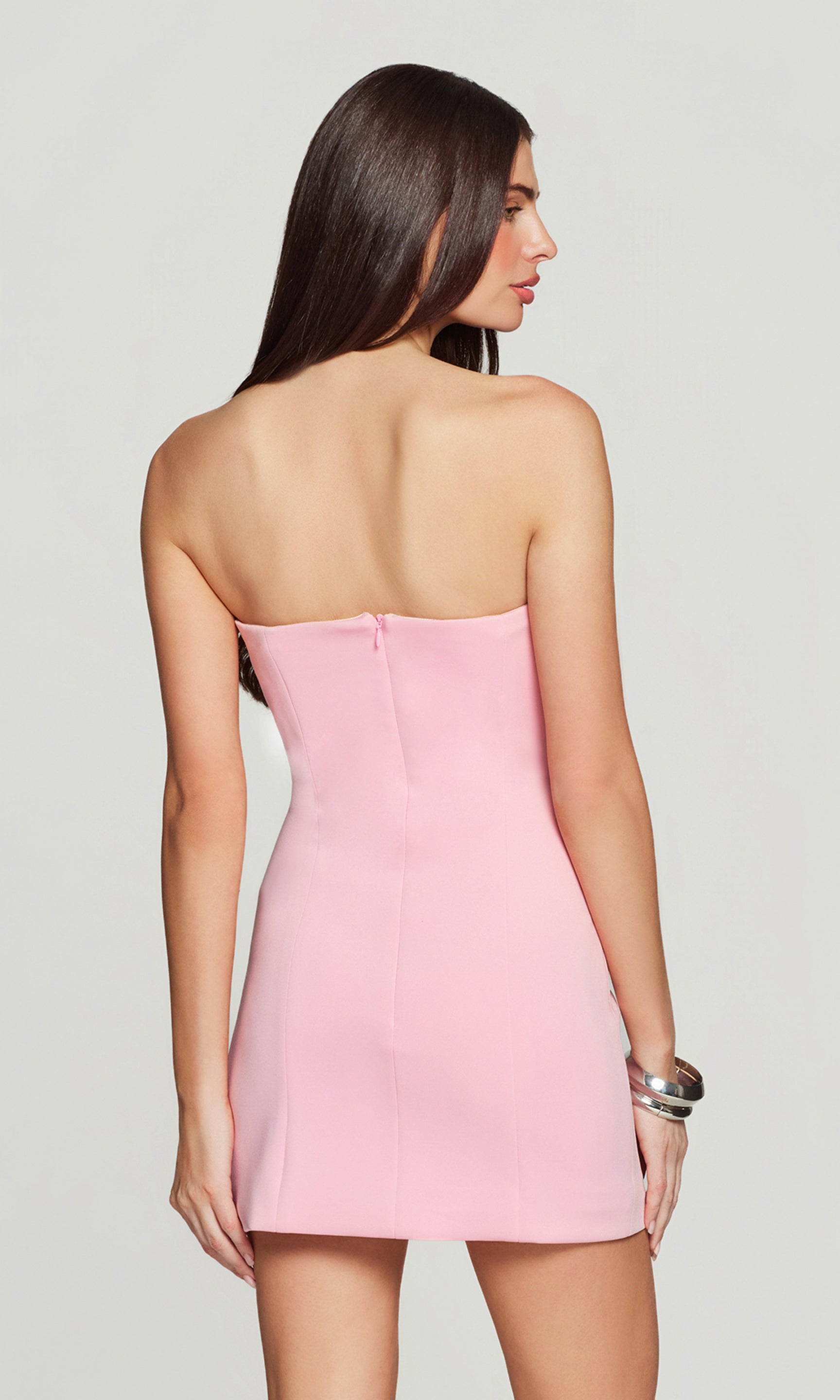 Back view of woman wearing a pink strapless dress against a plain background