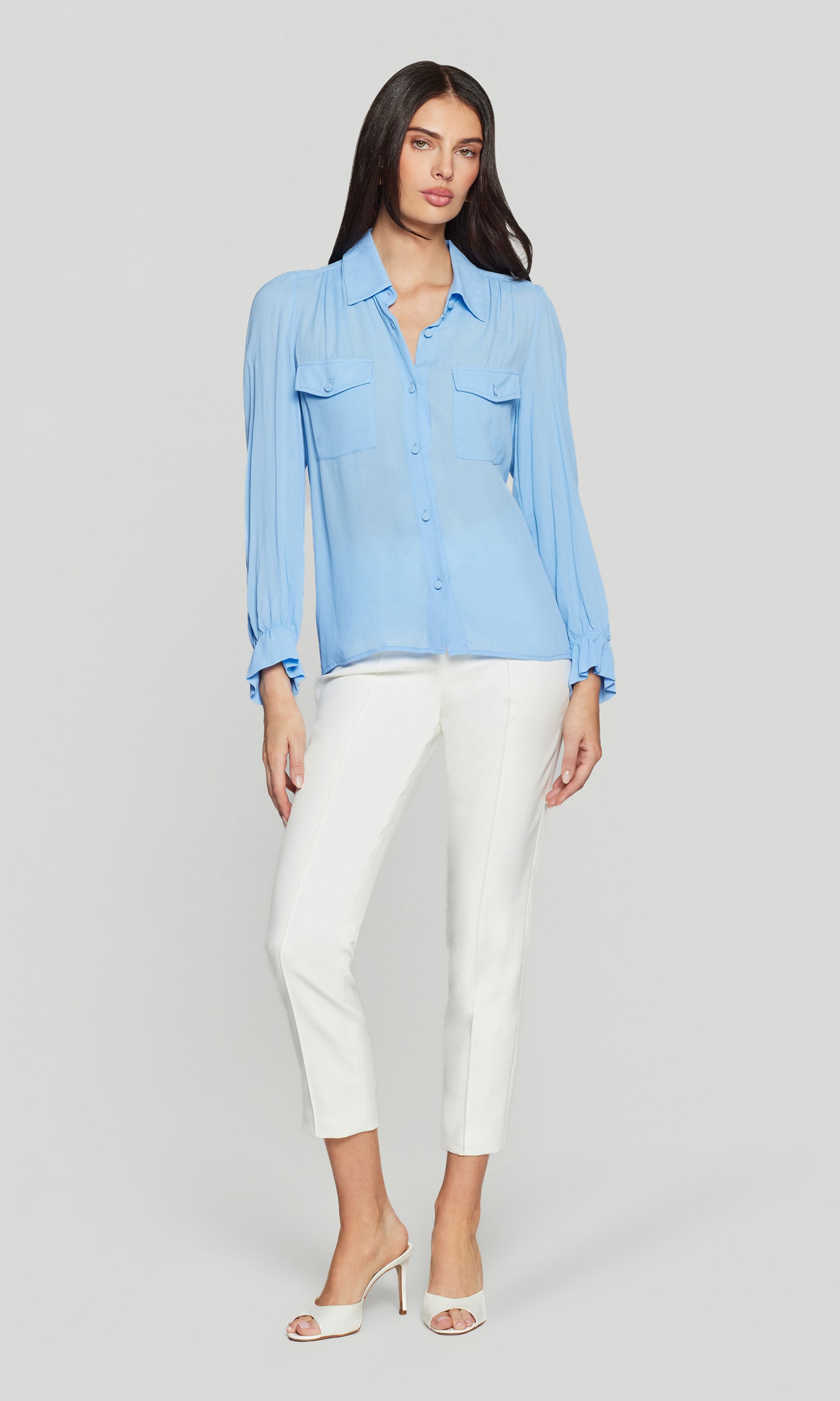 Model wears the Priya Georgette Shirt in light blue in a full-body front view, showing the lightweight drape and how the blouse sits with white pants and heels