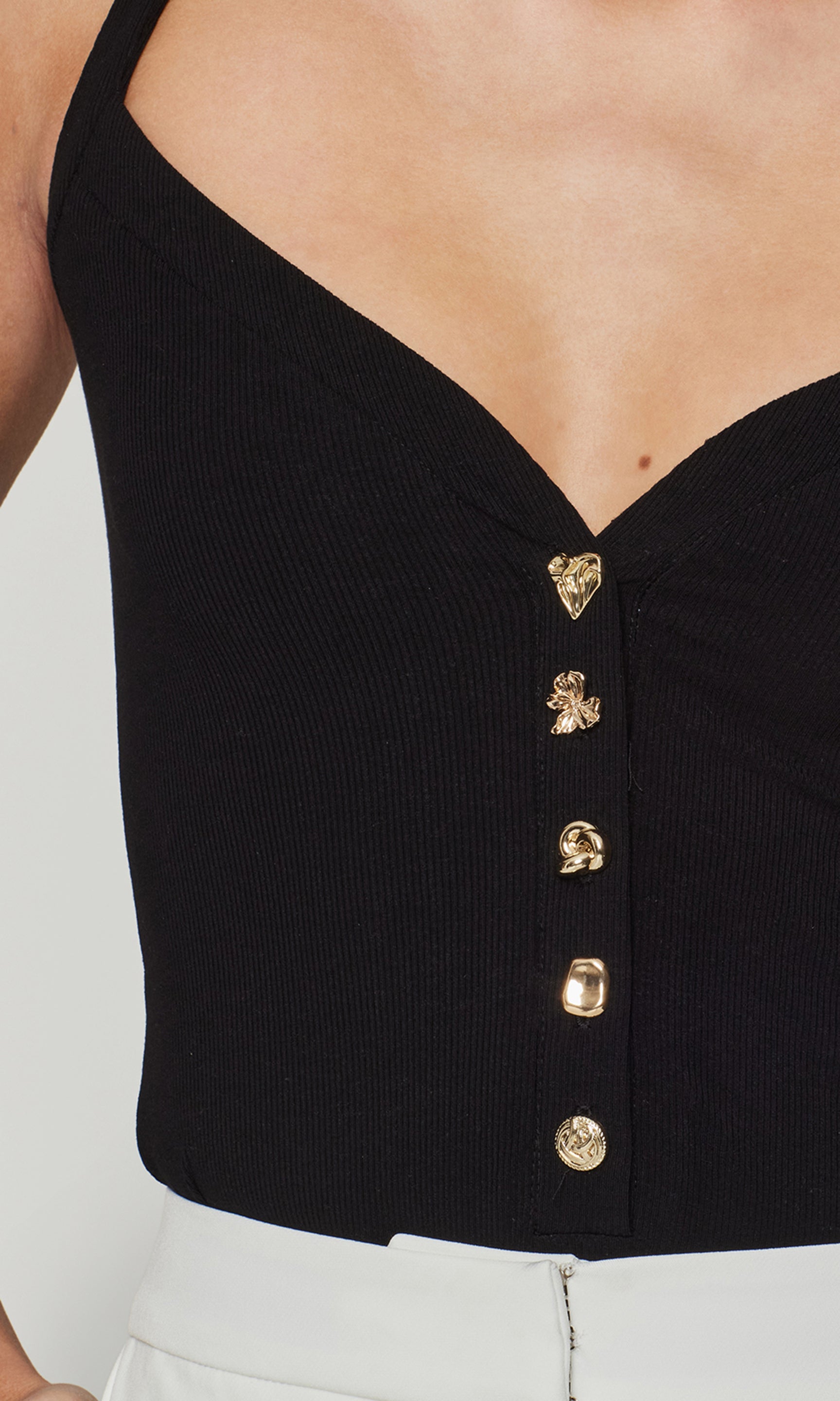 Close-up of black top with 5 different gold buttons on a plain background
