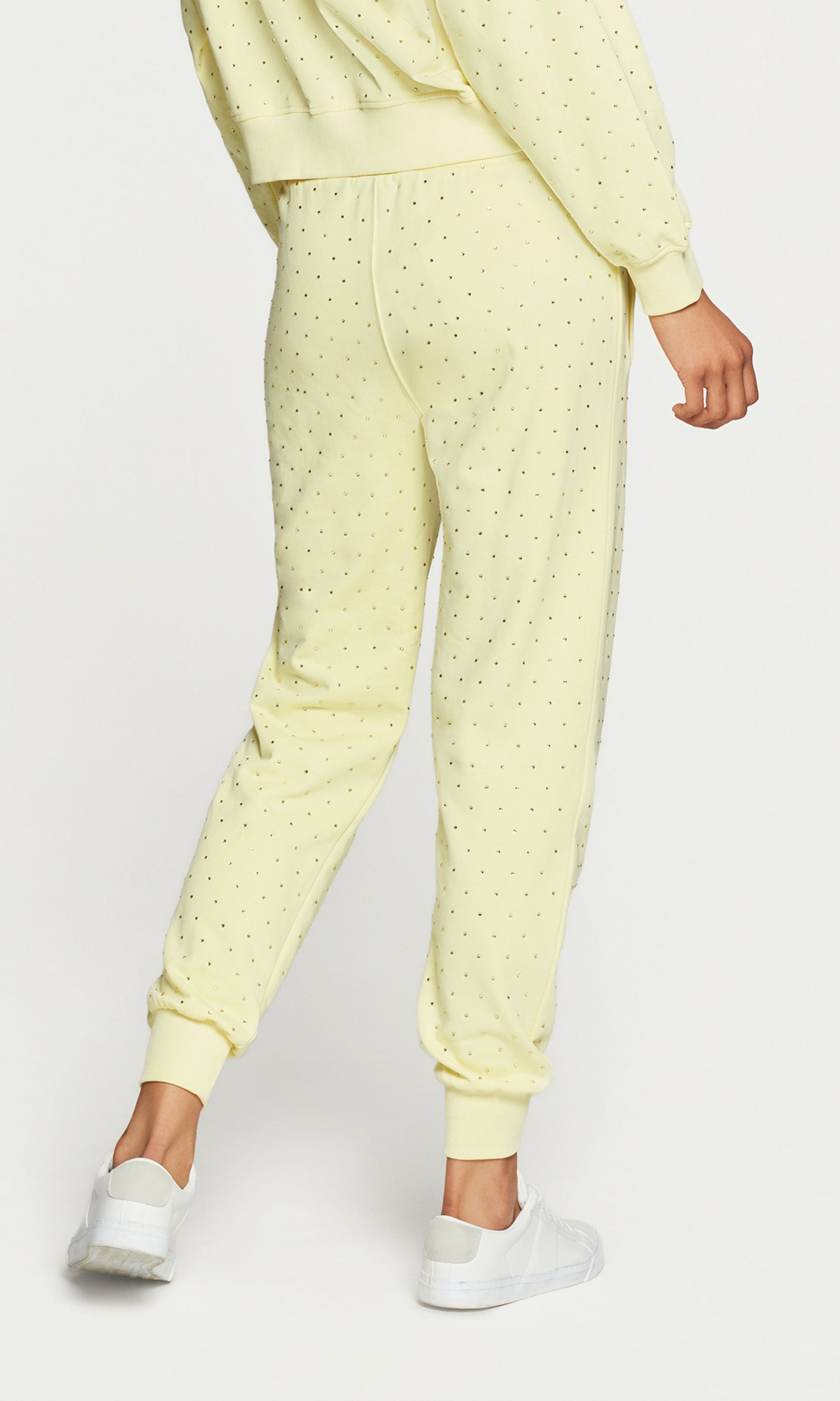 Back view of person wearing a yellow crystal embellished pants with white sneakers on a light gray background