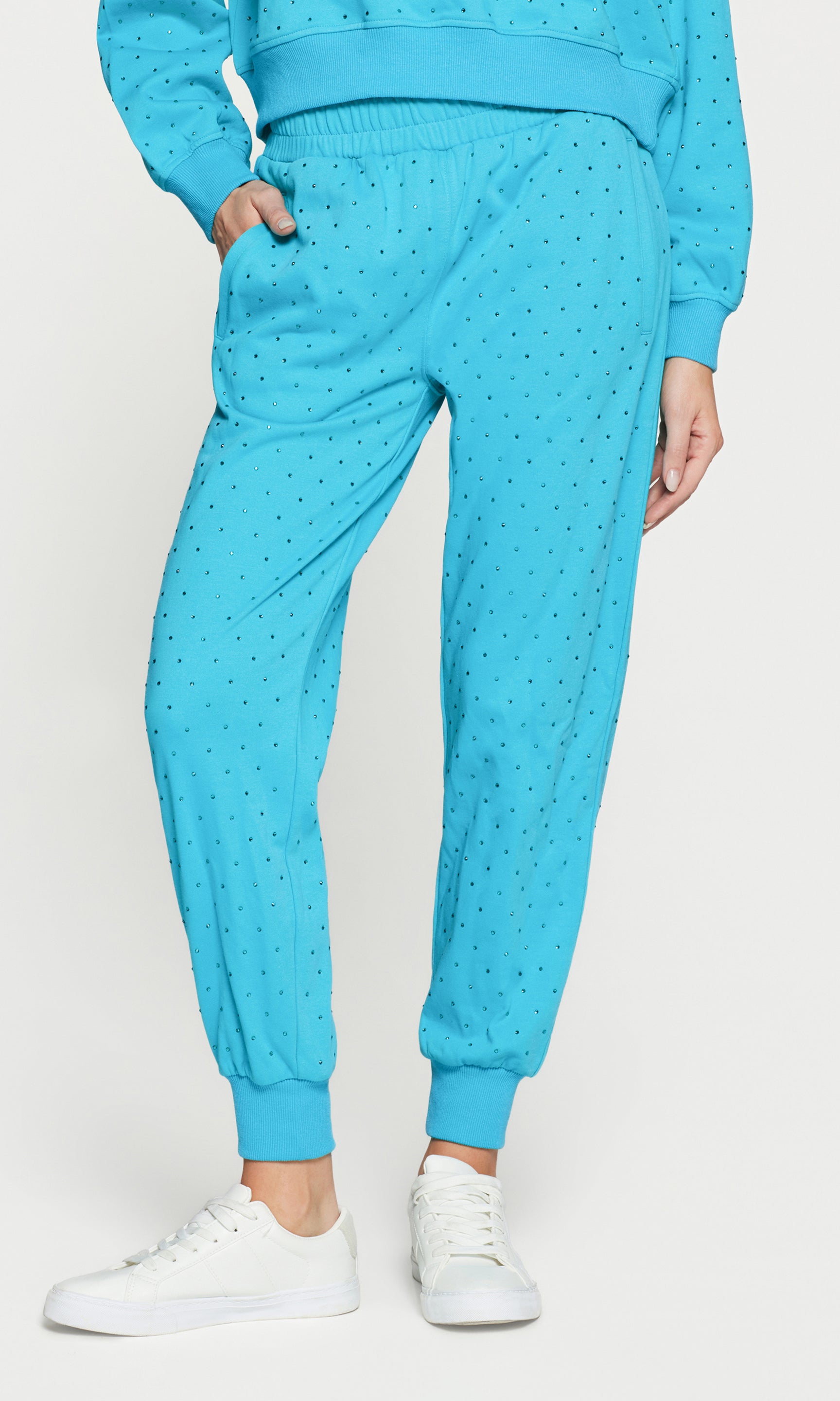 Person wearing a blue crystal embellished pants with white sneakers on a white background