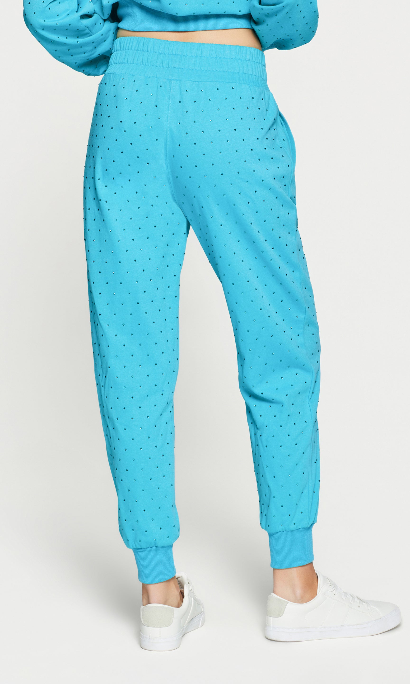 Back view of person wearing a blue crystal embellished pants with white sneakers on a white background