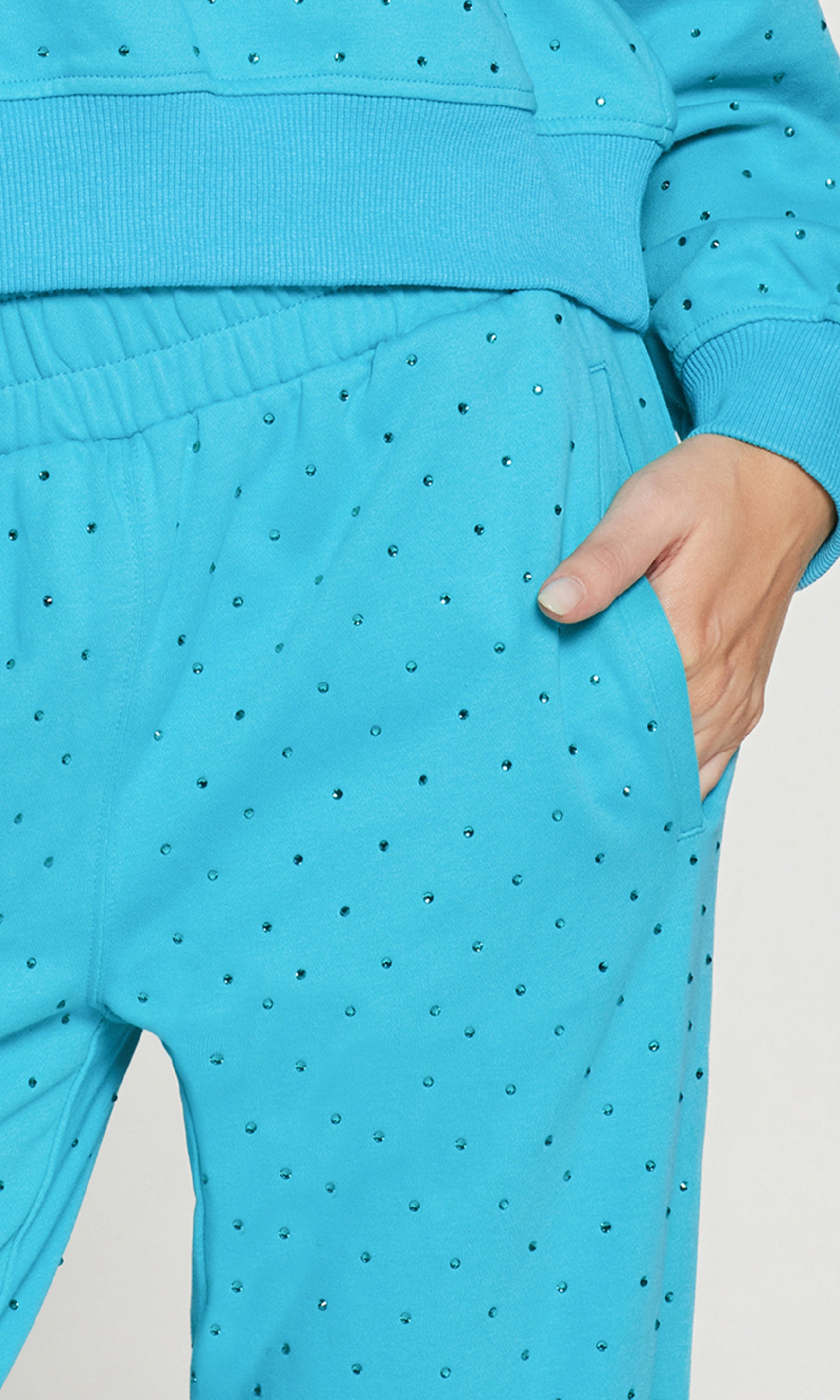 Close-up of person wearing a blue crystal embellished pants with white sneakers on a white background