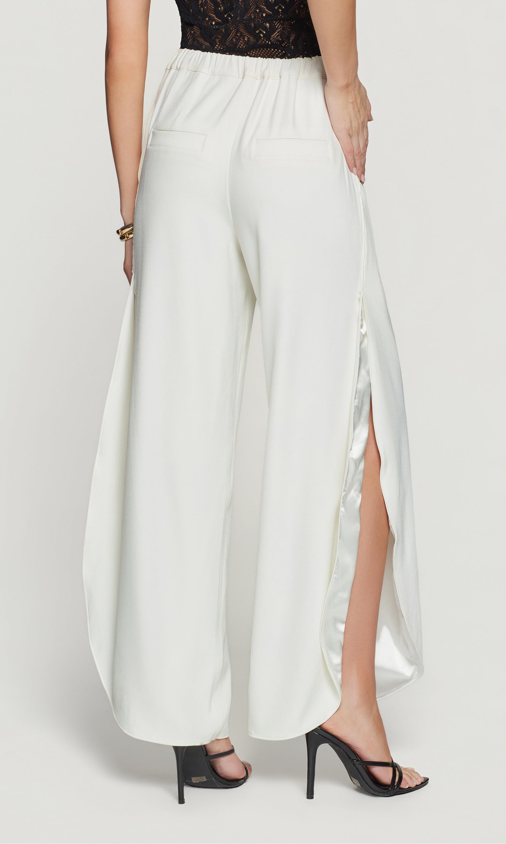 Back view of white wide-leg pants with a high slit worn by a person on a white background